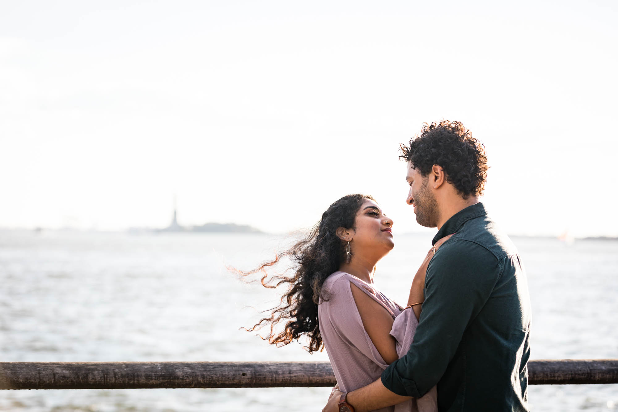 Battery Park engagement photos of couple hugging with Statue of Liberty in background