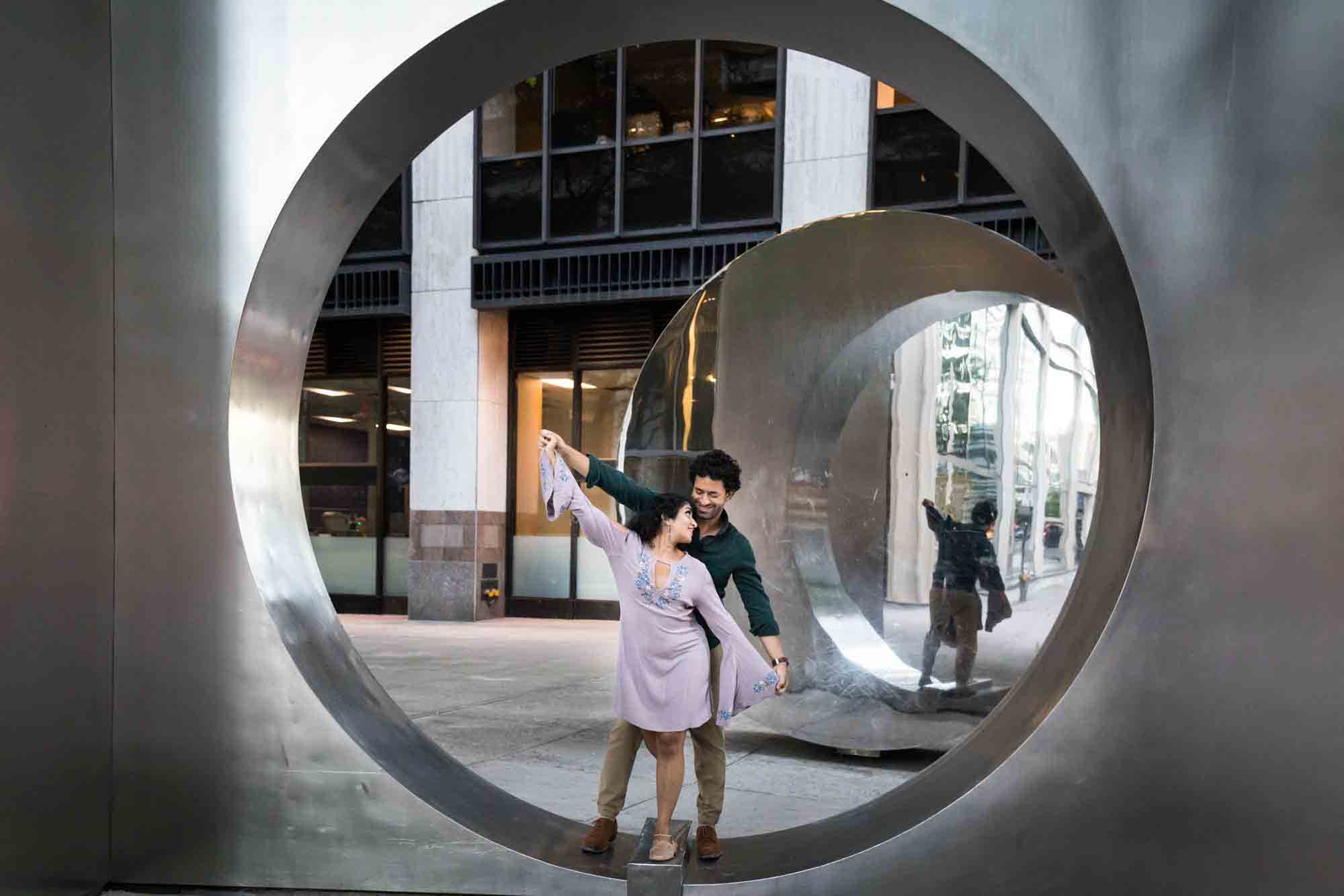 Couple dancing in circle of metallic sculpture in NYC