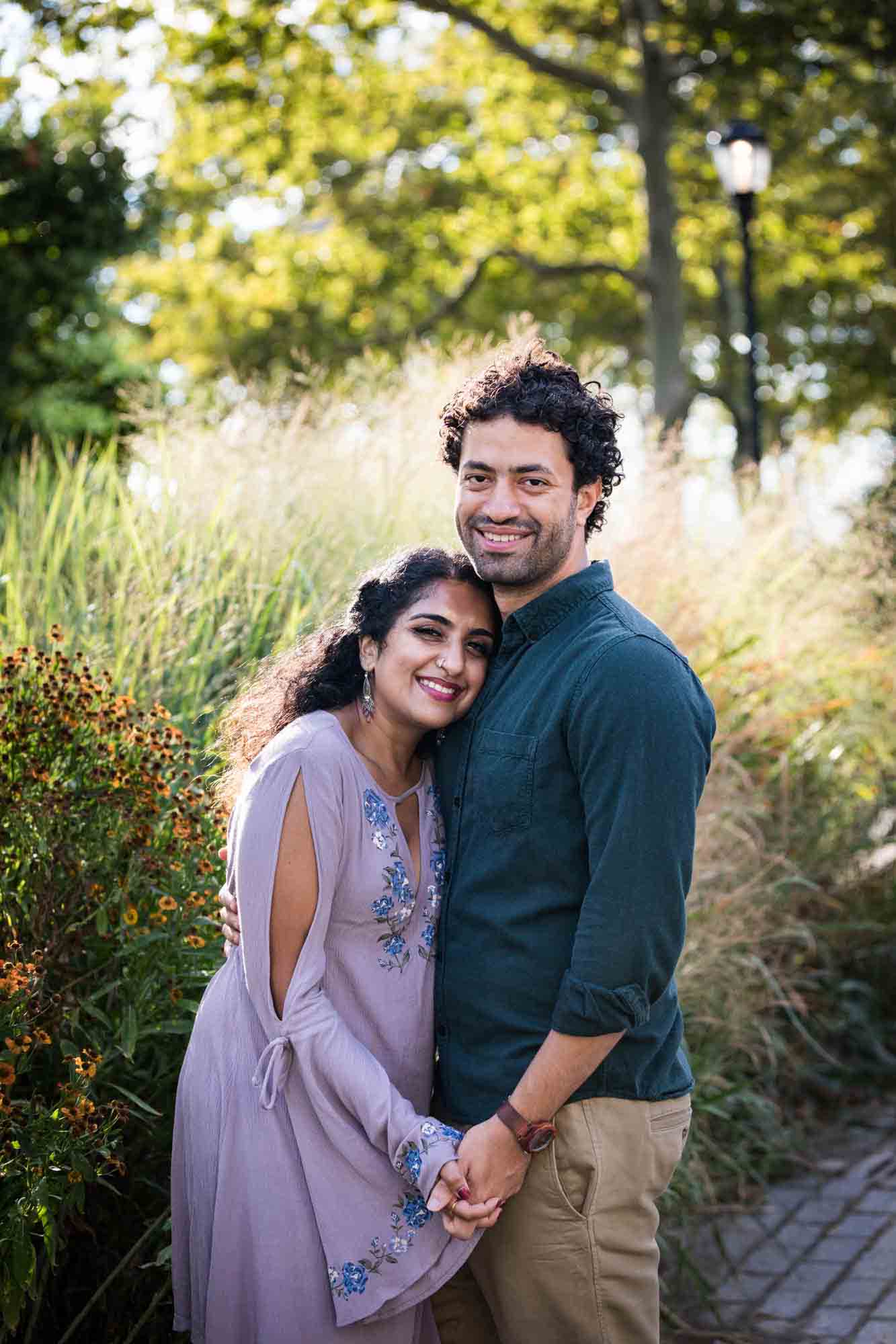 Battery Park engagement photos of couple hugging in front of tall bushes