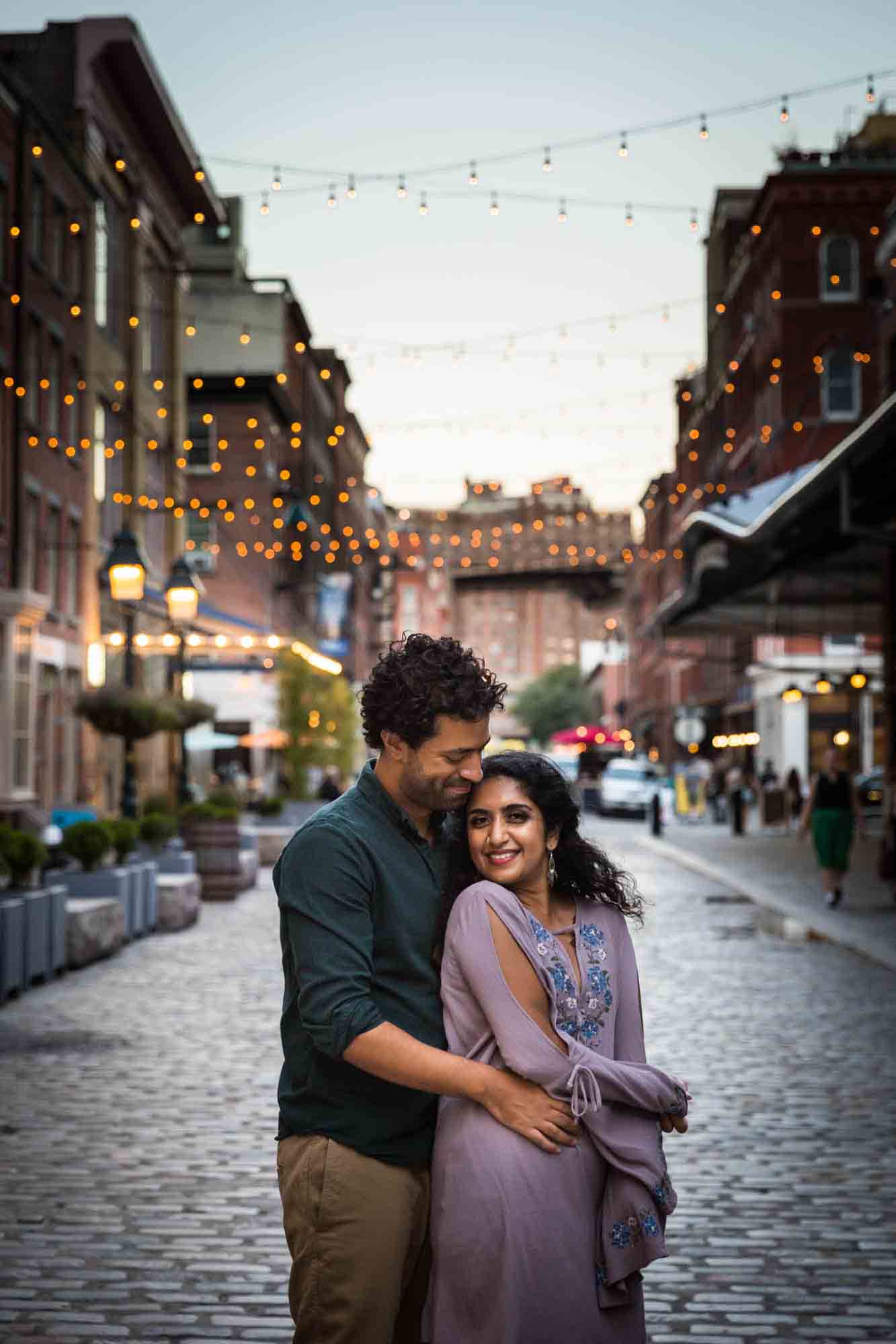 Couple hugging under fairy lights on Front Street in South Street Seaport