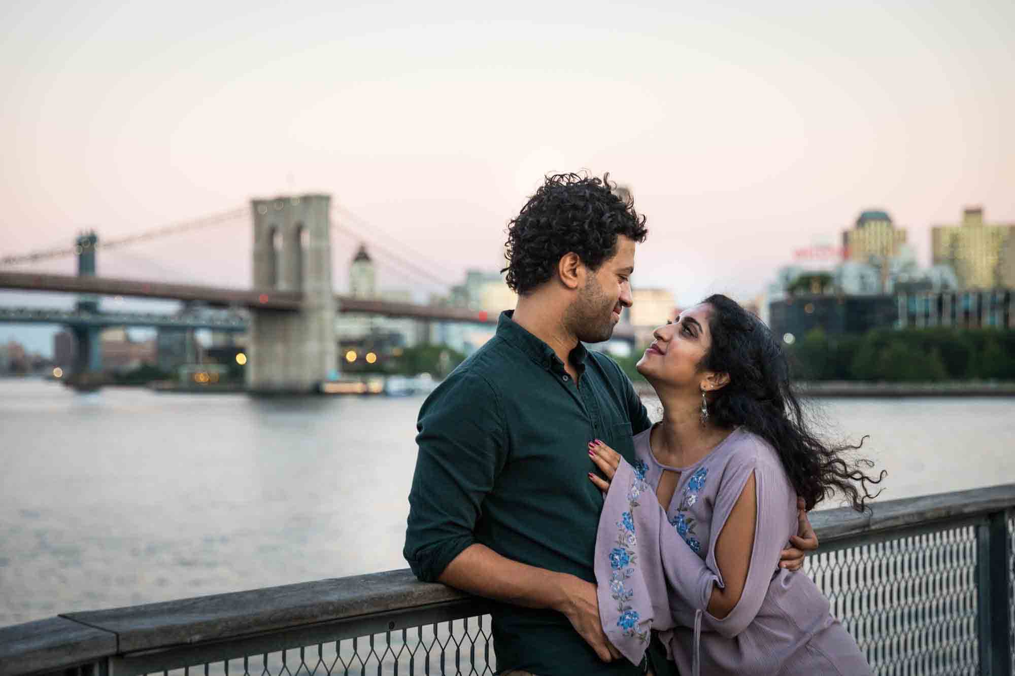 Couple hugging on Pier 17 with Brooklyn Bridge at sunset in background