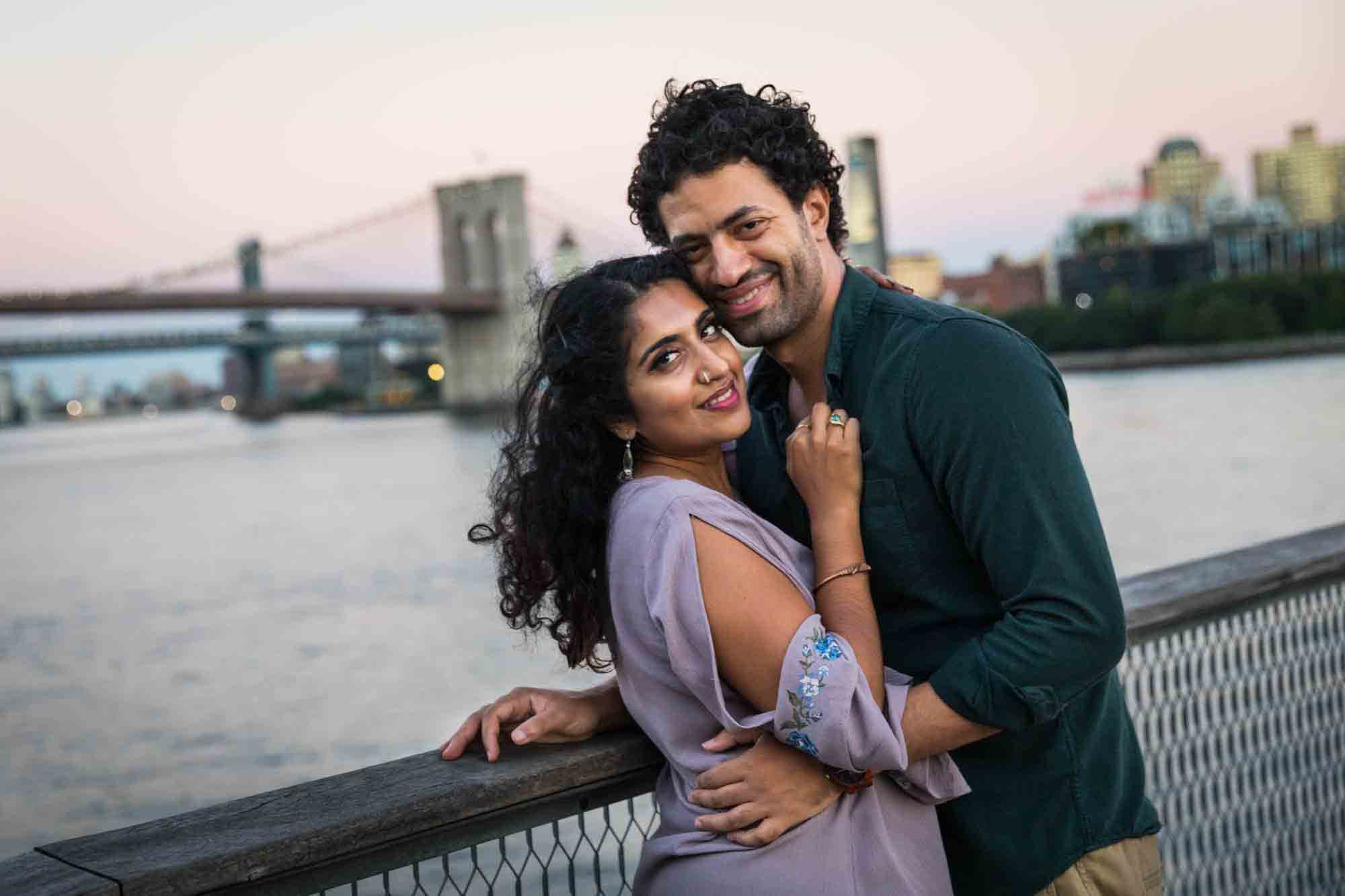 Battery Park engagement photos of couple hugging with Brooklyn Bridge at sunset in the background