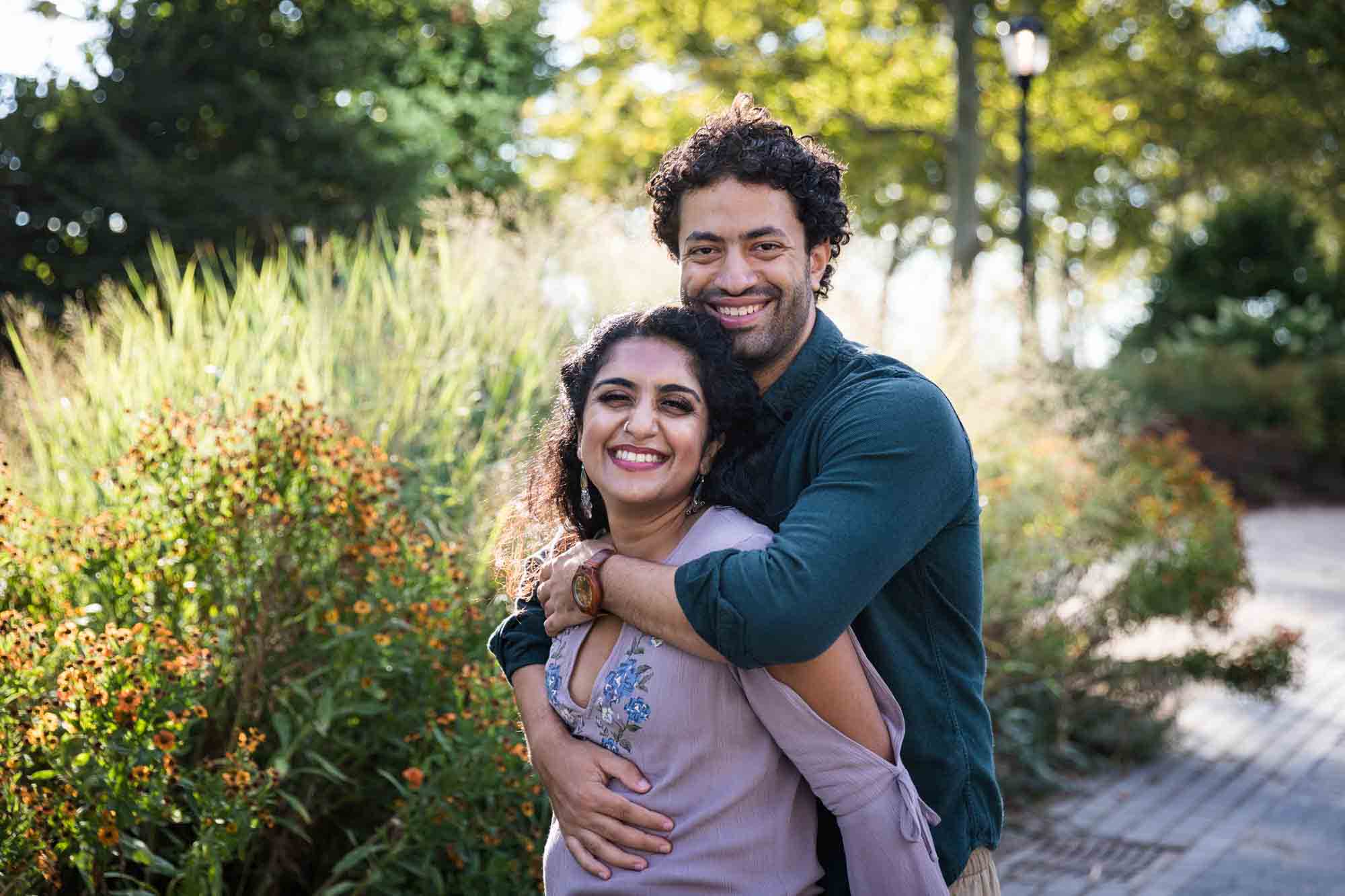 Battery Park engagement photos of man hugging woman from behind in front of tall grass