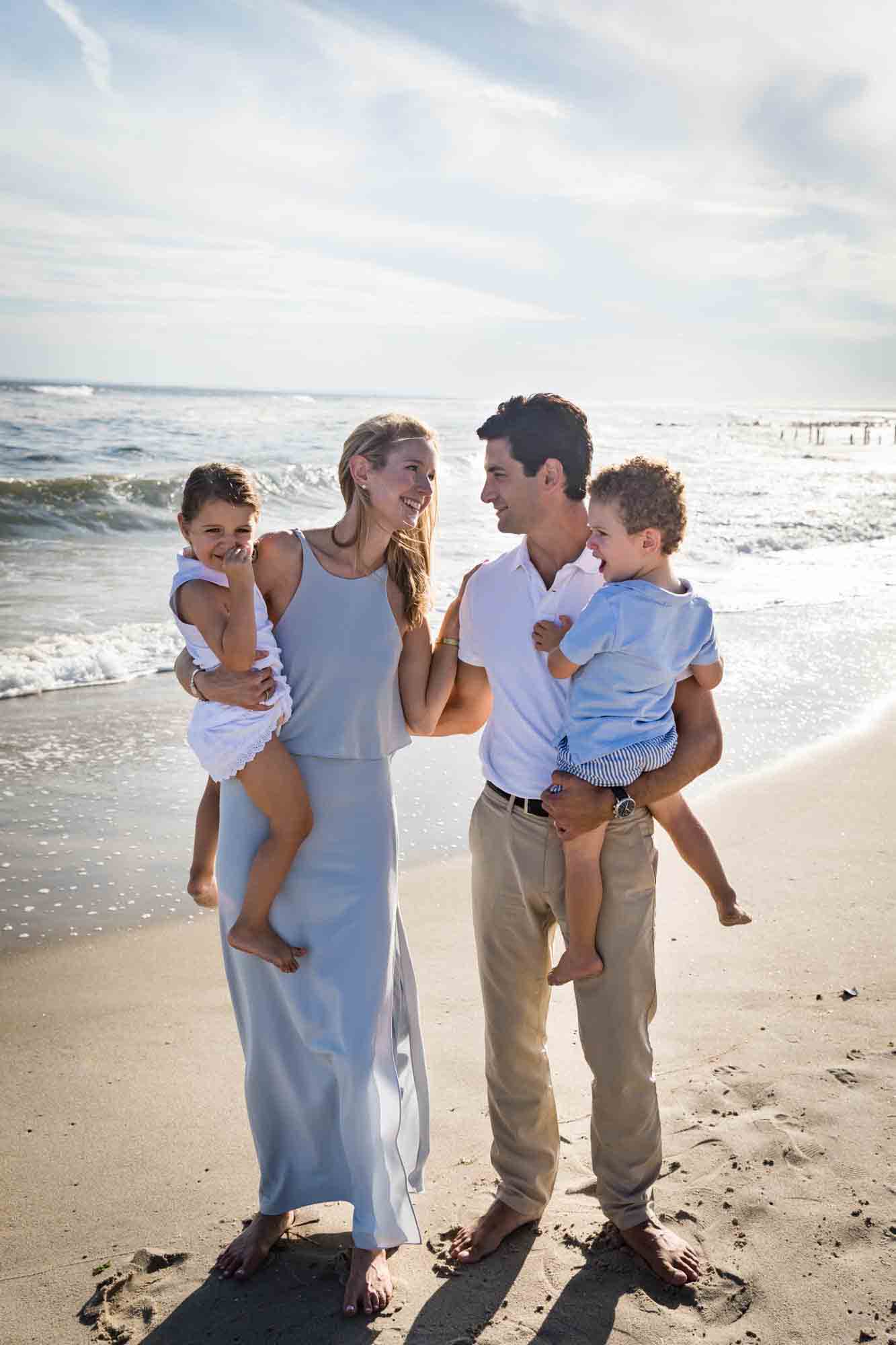 Parents holding two small children on beach in front of ocean for an article on beach family portrait tips