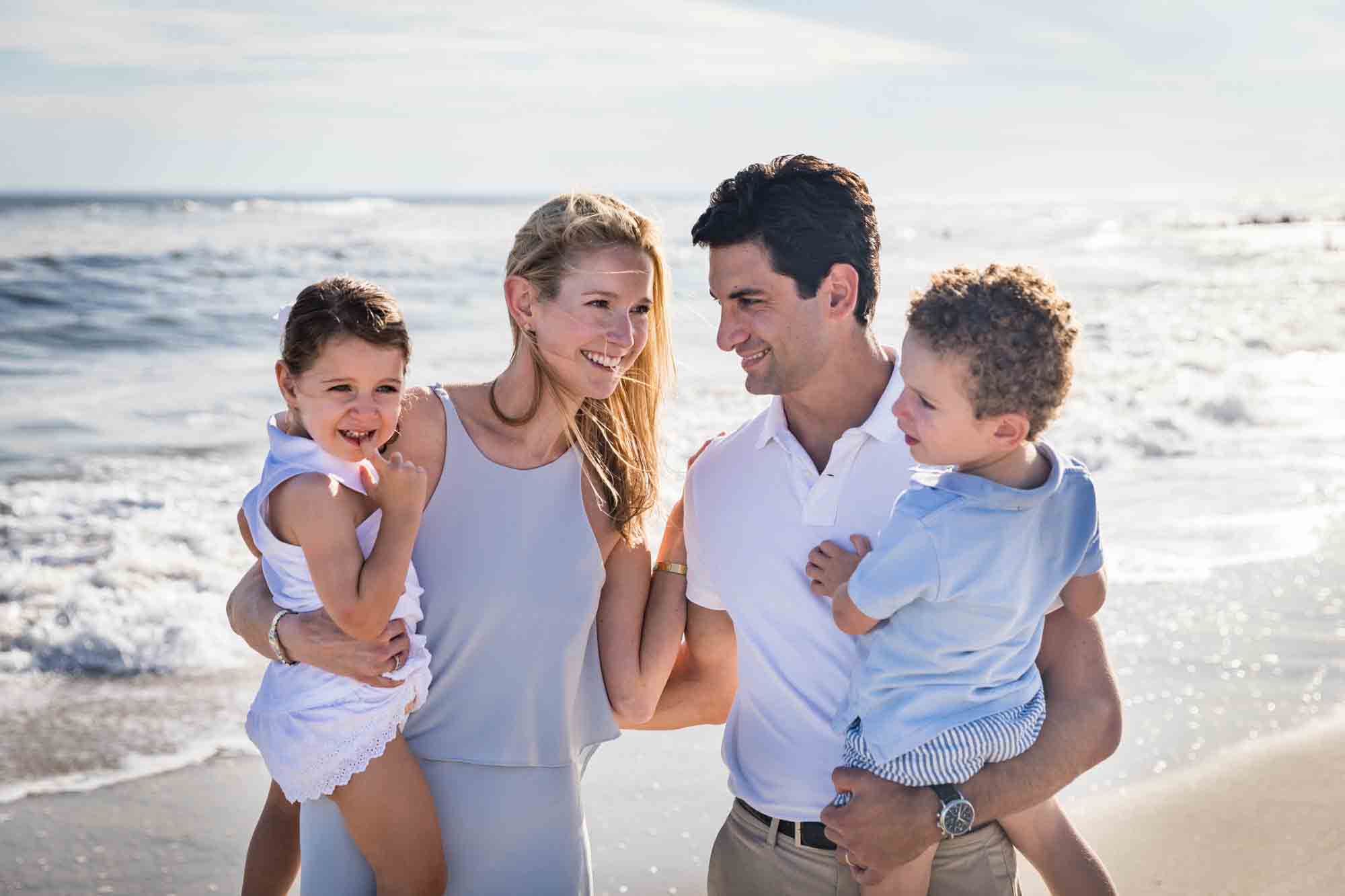 Parents holding two small children on beach in front of ocean for an article on beach family portrait tips