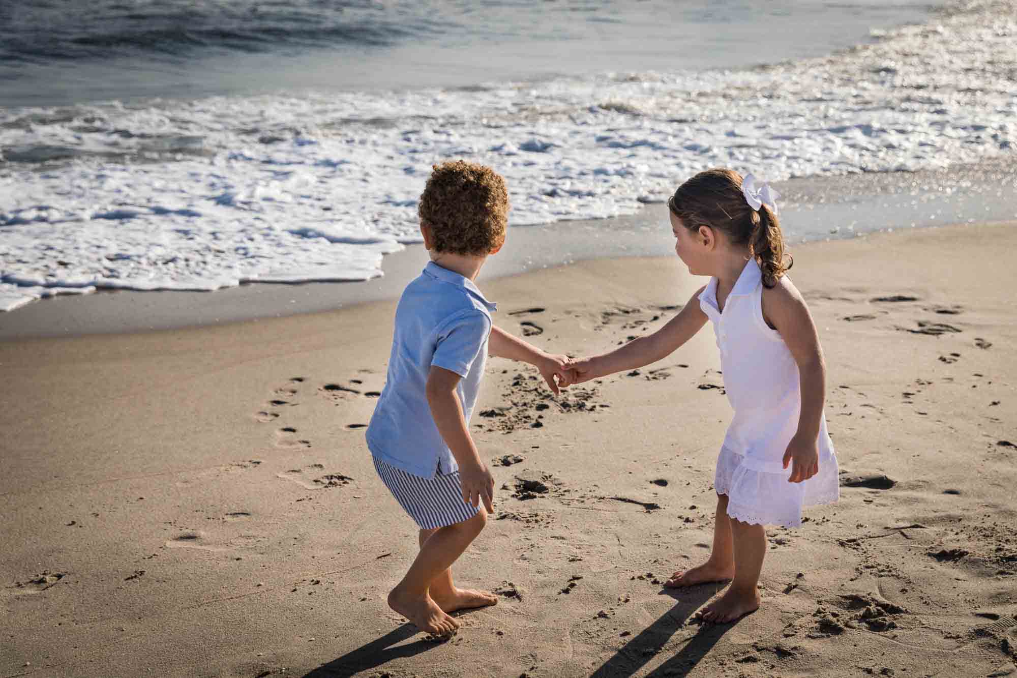 Fort Tilden beach family portrait of two small children holding hands and looking back at the ocean