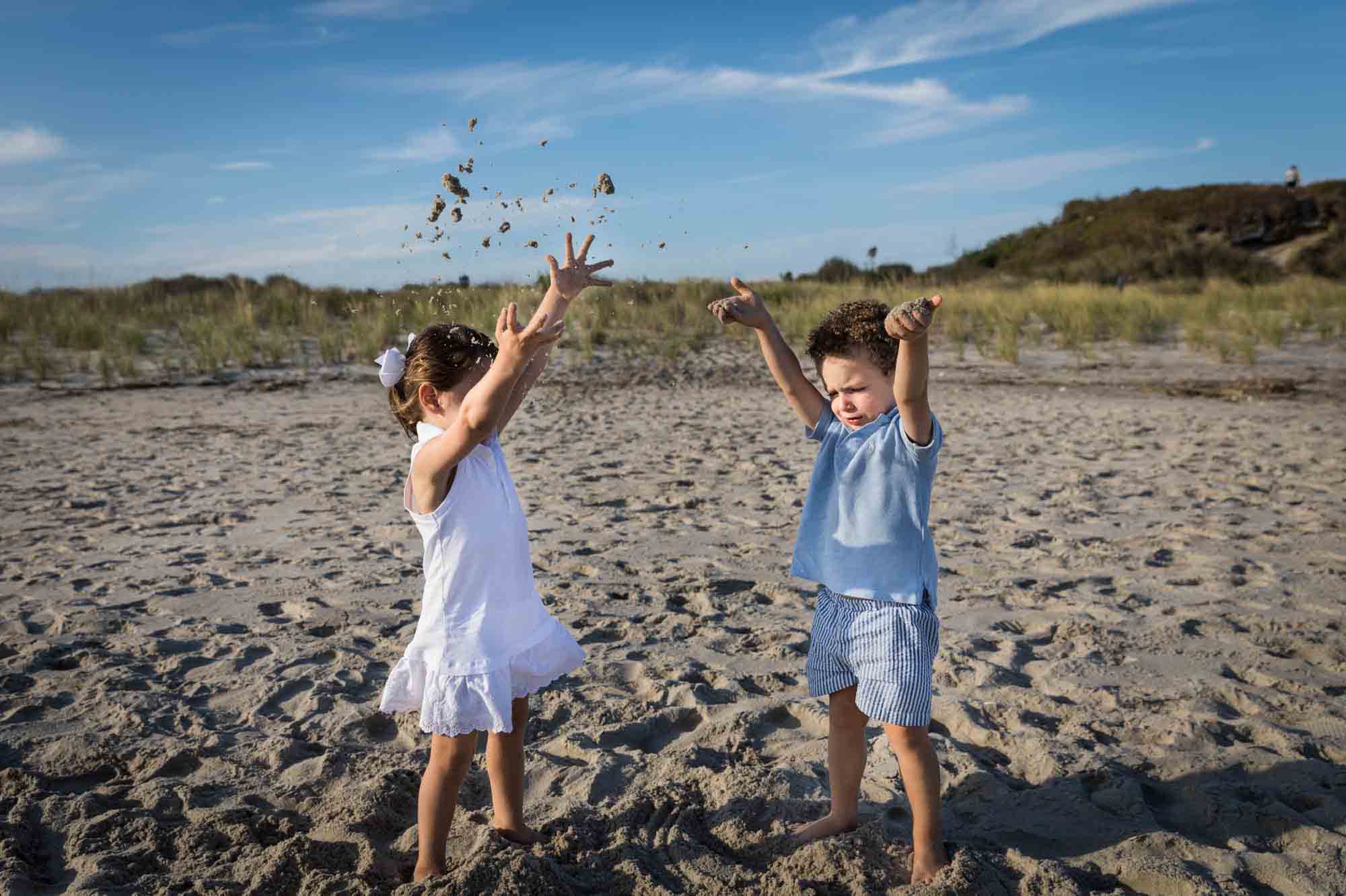 Two small children throwing sand in the air on a beach for an article on beach family portrait tips