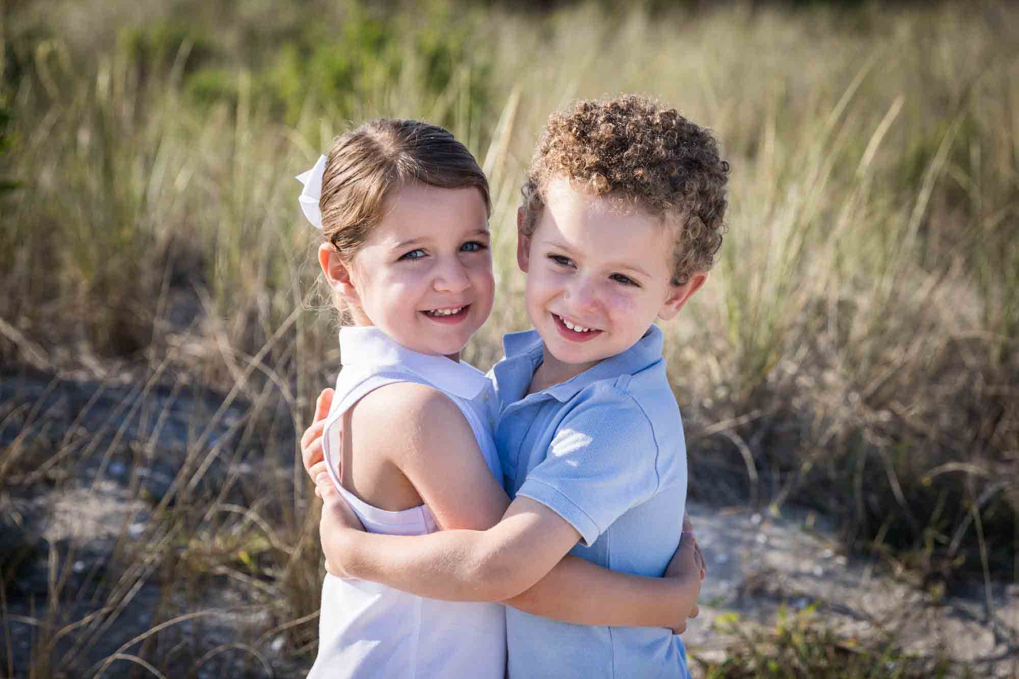 Two children hugging on a beach in front of dunes for an article on beach family portrait tips