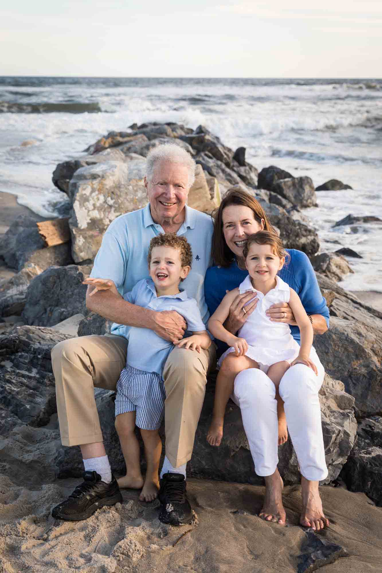 Fort Tilden family portrait of grandparents with two small children sitting on jetty in front of ocean