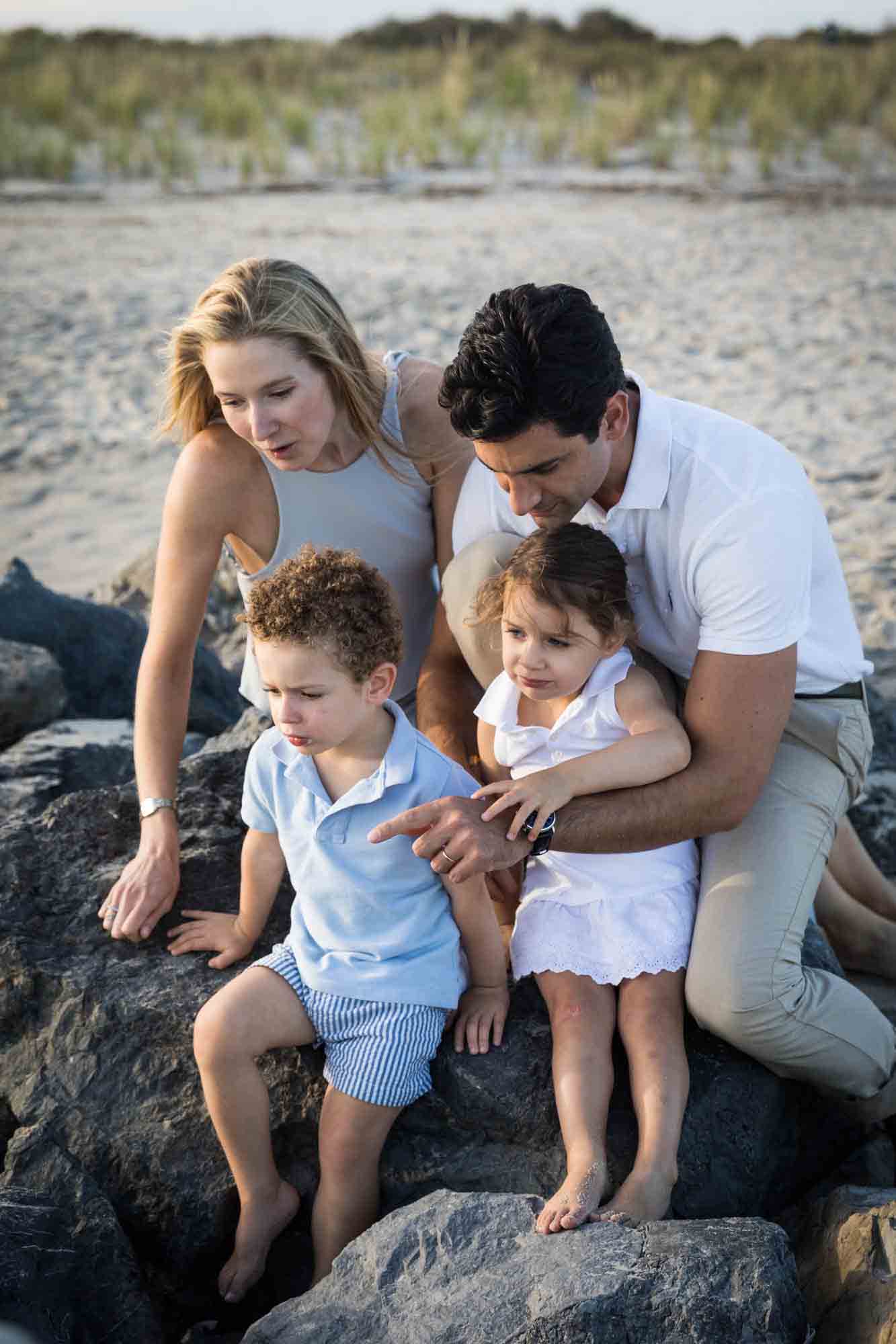 Fort Tilden family portrait of family with two kids sitting on jetty looking at something