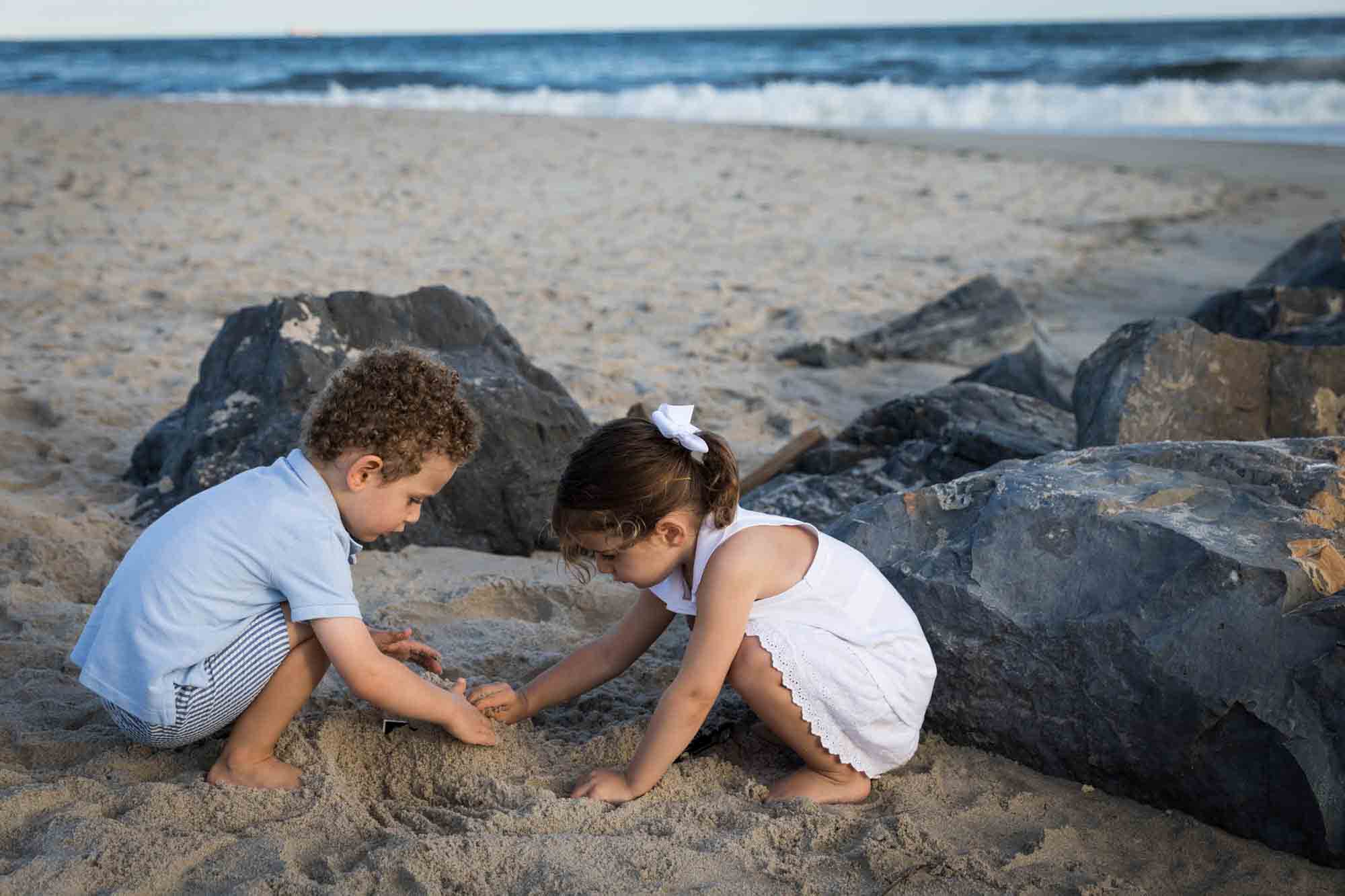 Beach family portrait of two children playing in sand in front of rocks