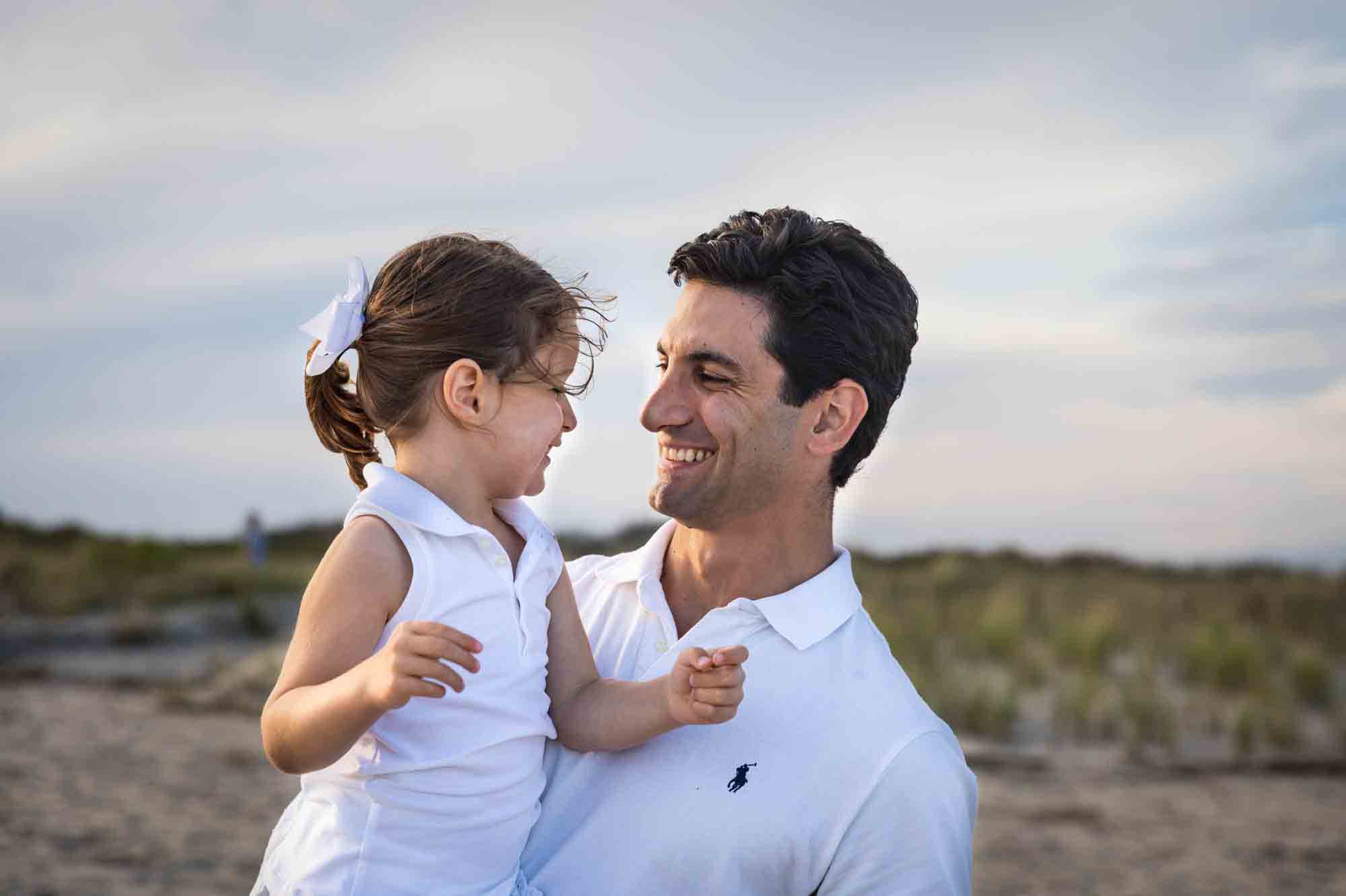 Beach family portrait of father holding small girl in front of sand dunes