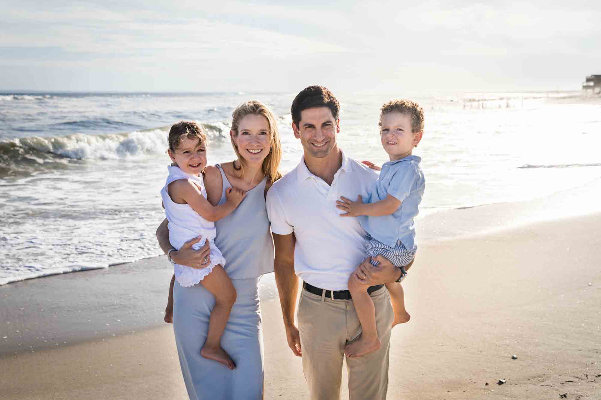 Parents holding two small children on beach in front of ocean for an article on beach family portrait tips