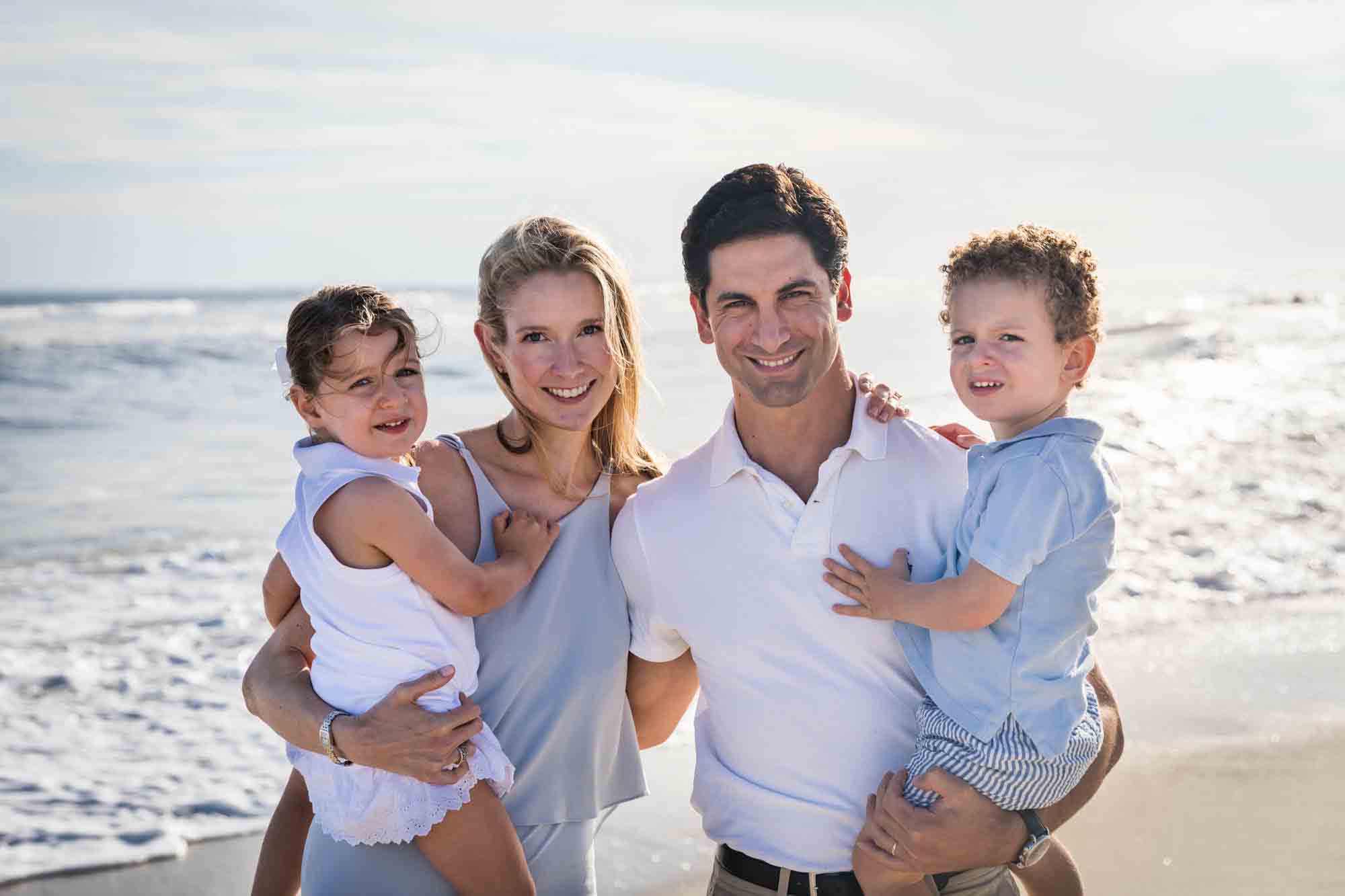 Parents holding two small children on beach in front of ocean for an article on beach family portrait tips