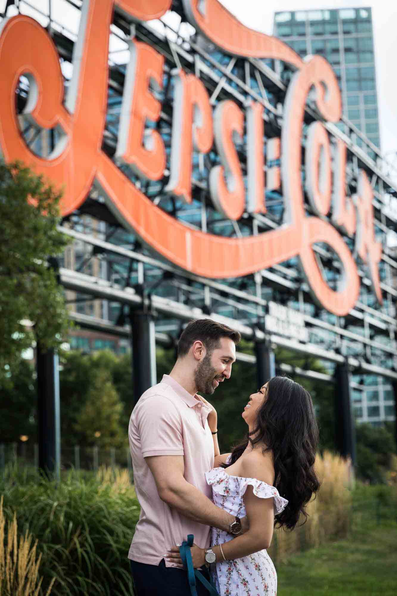 Couple hugging in front of Pepsi Cola neon sign during a Gantry Plaza State Park engagement photo shoot