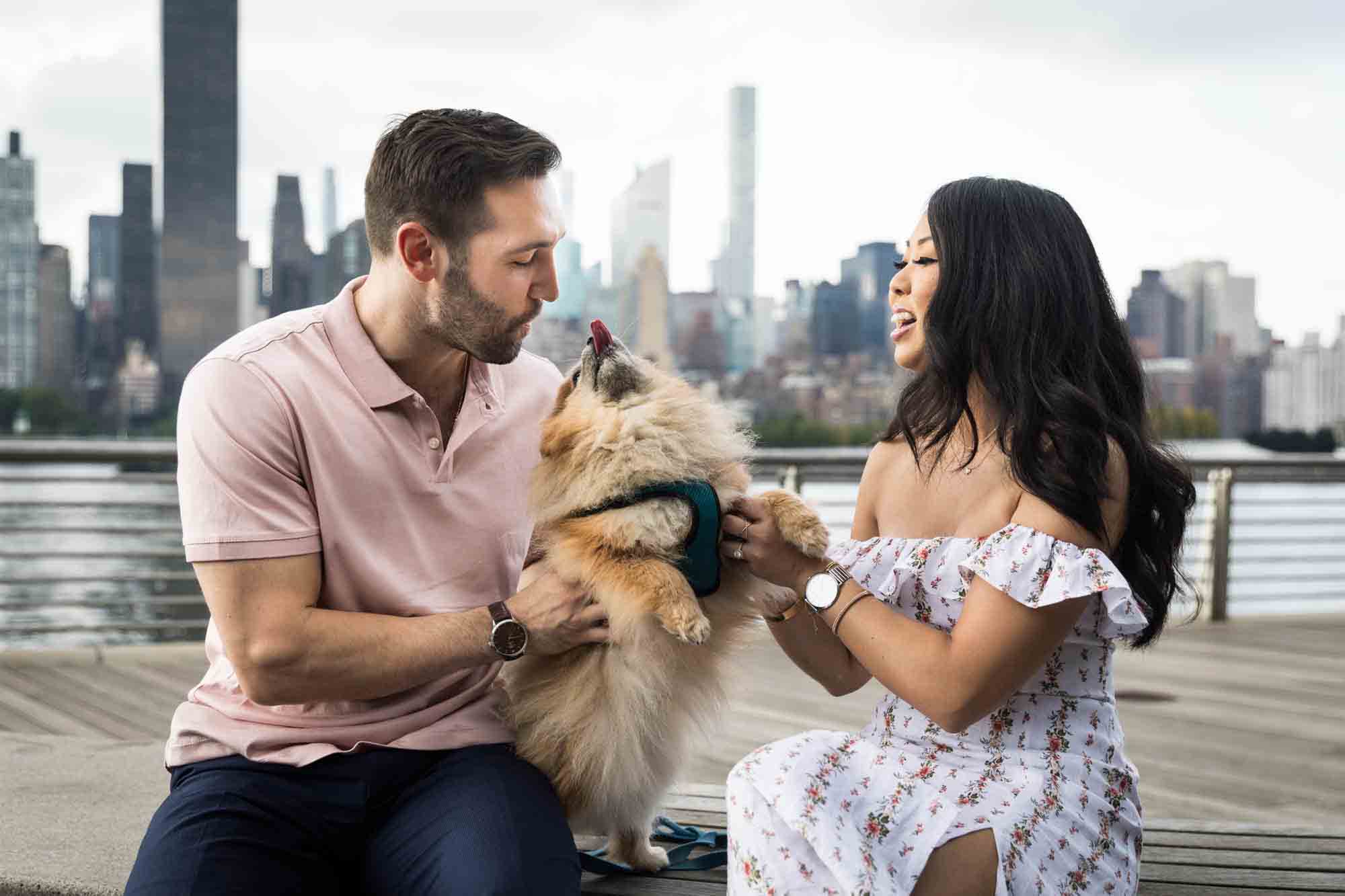 Couple playing with Pomeranian during Gantry Plaza State Park engagement session for an article on engagement portrait clothing tips