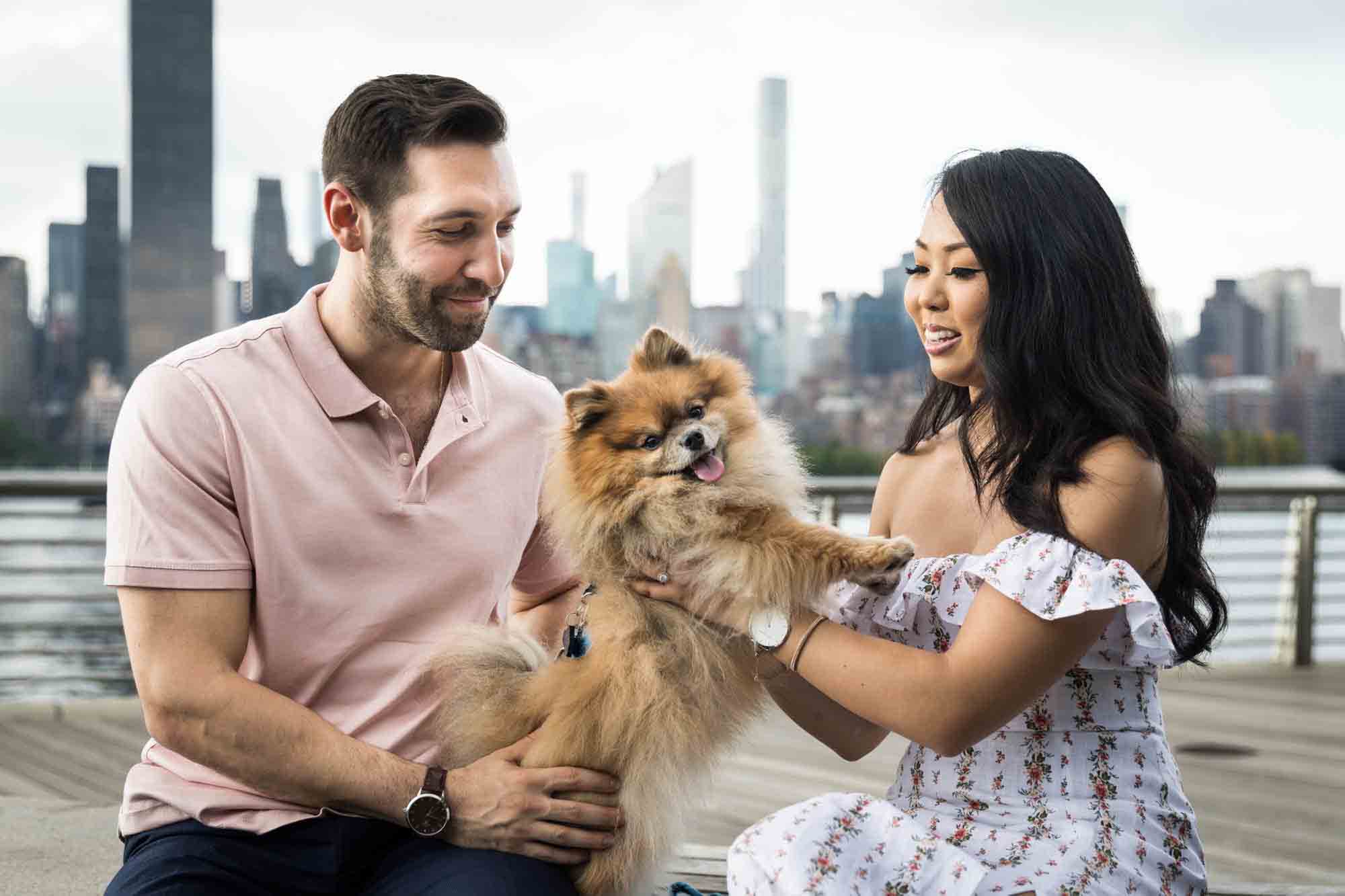 Couple playing with Pomeranian during a Gantry Plaza State Park engagement photo shoot