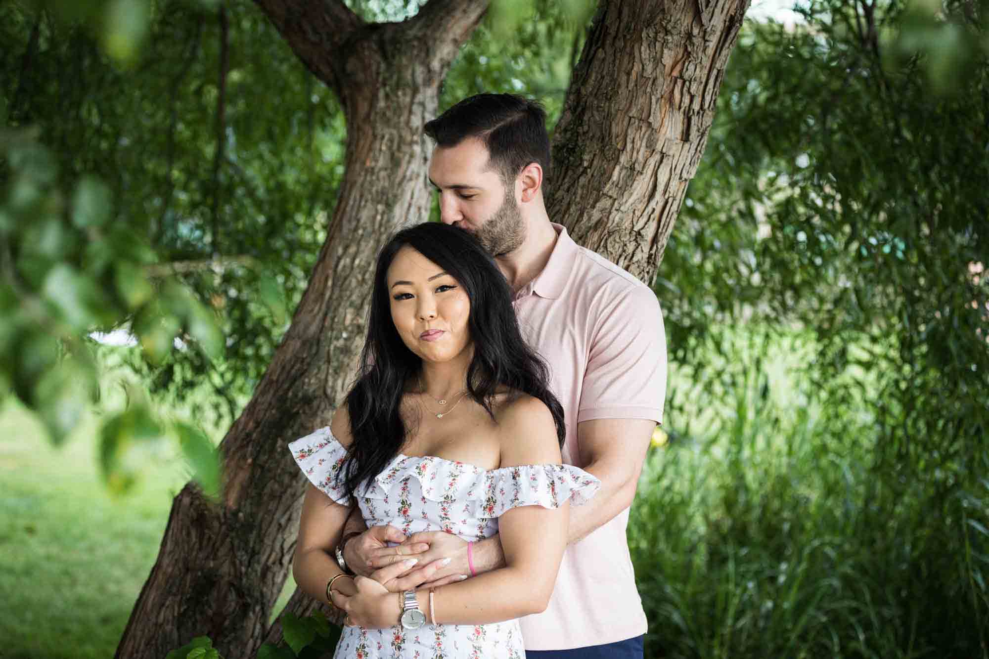 Couple hugging in front of tree during a Gantry Plaza State Park engagement photo shoot