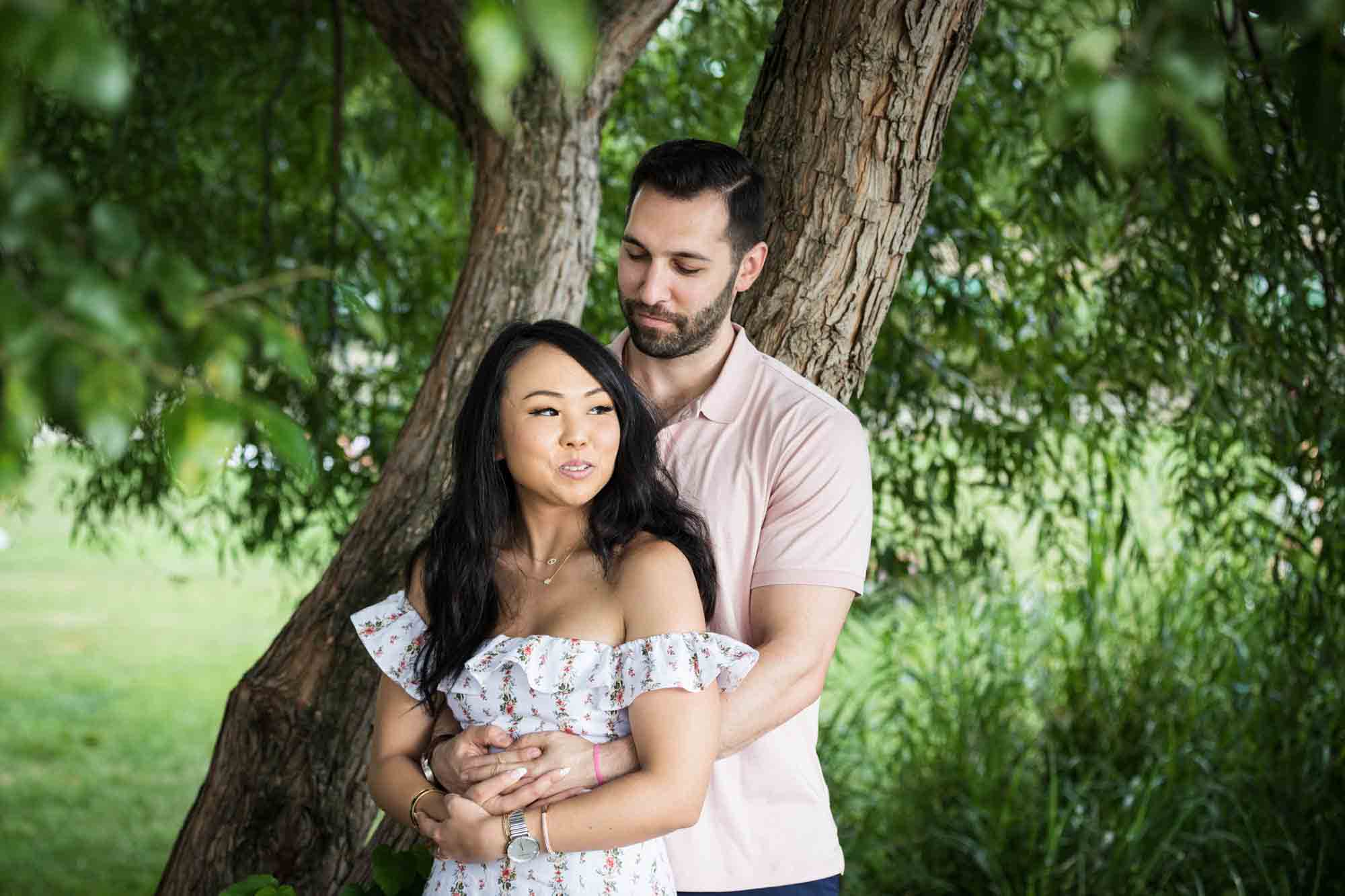 Couple hugging under tree during Gantry Plaza State Park engagement session for an article on engagement portrait clothing tips