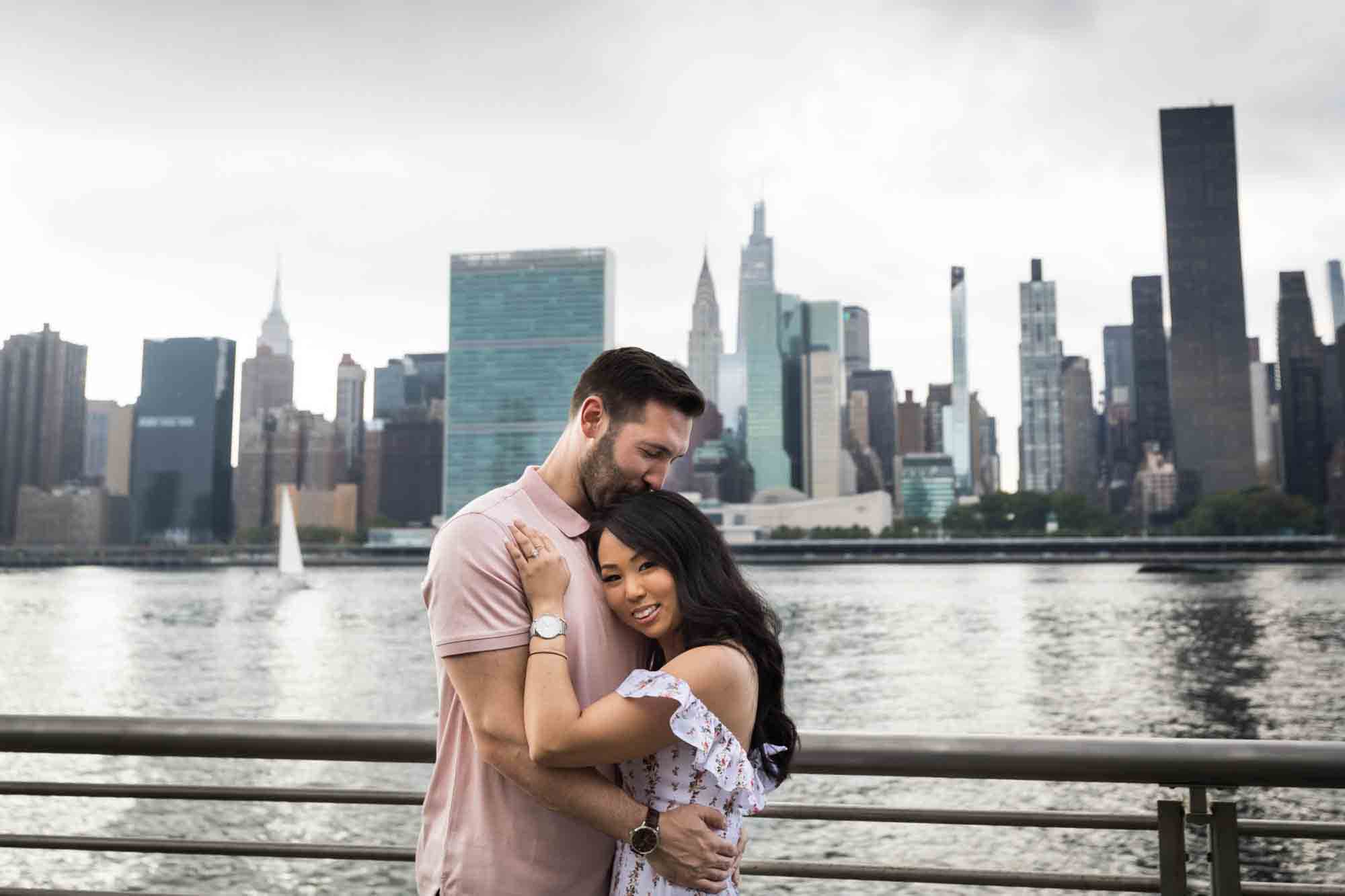 Couple hugging in front of NYC waterfront during a Gantry Plaza State Park engagement photo shoot