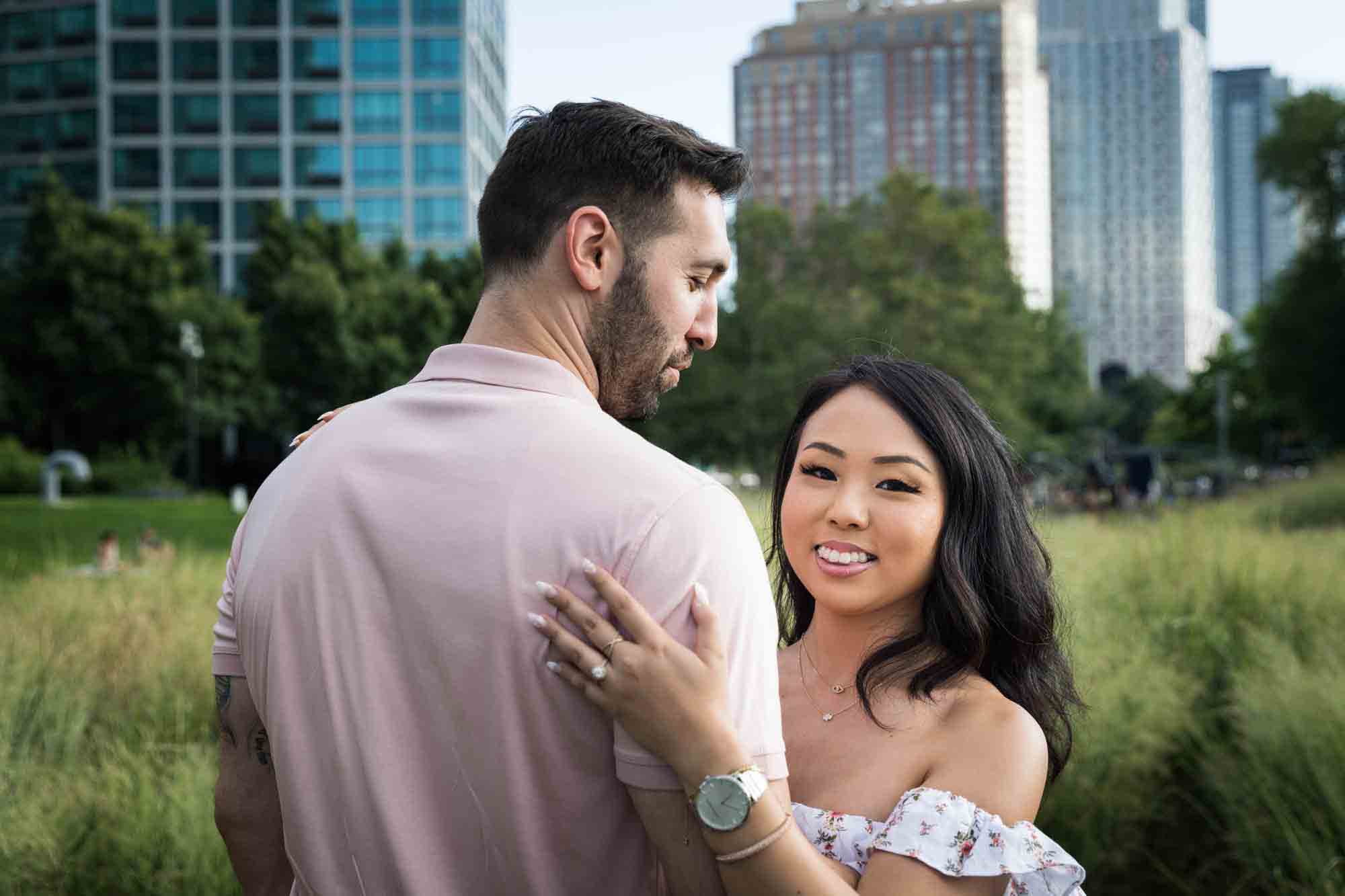 Woman hugging man and showing rose gold engagement ring during a Gantry Plaza State Park engagement photo shoot