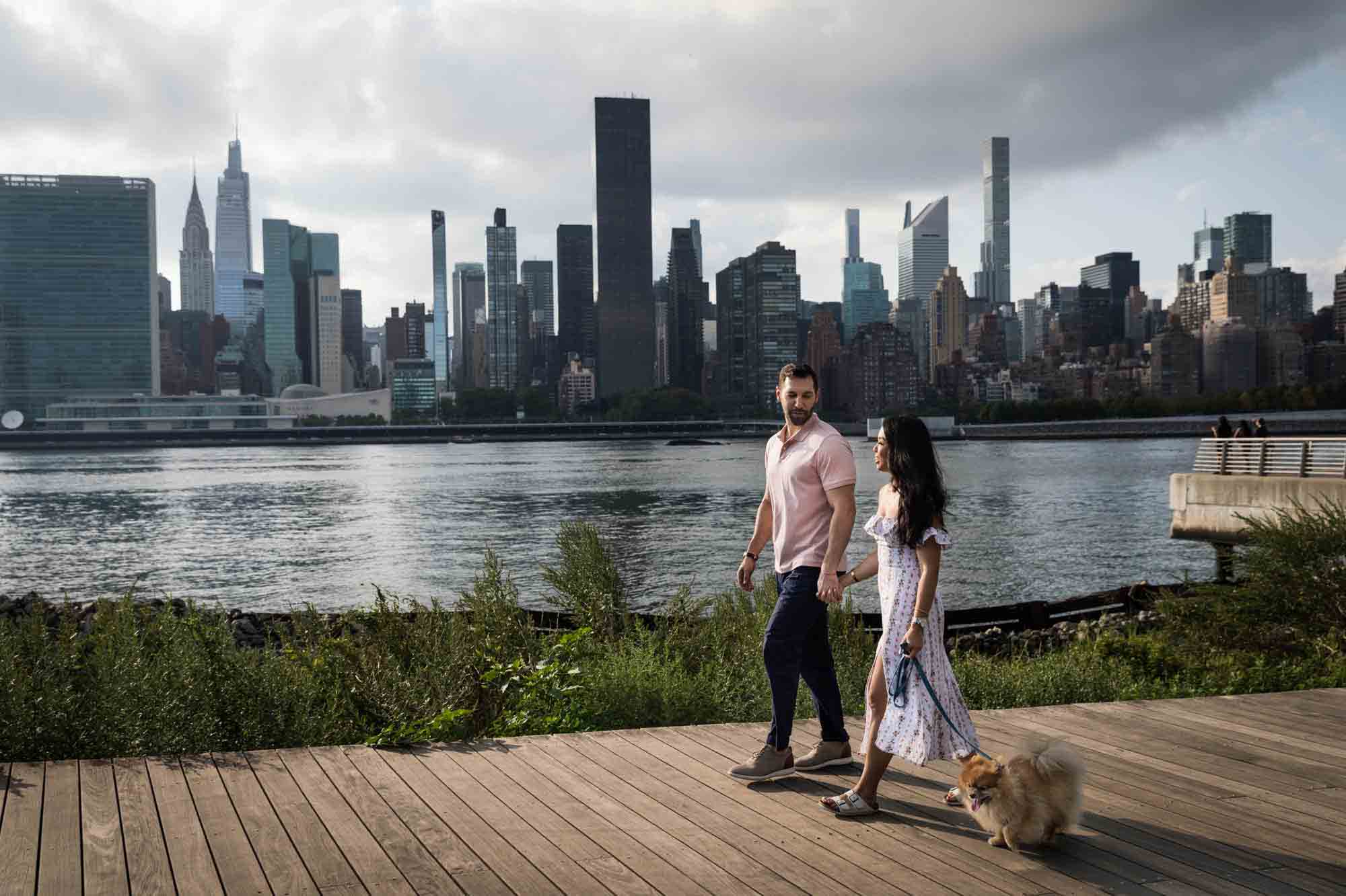 Couple walking on backlit in front of NYC waterfront during a Gantry Plaza State Park engagement photo shoot