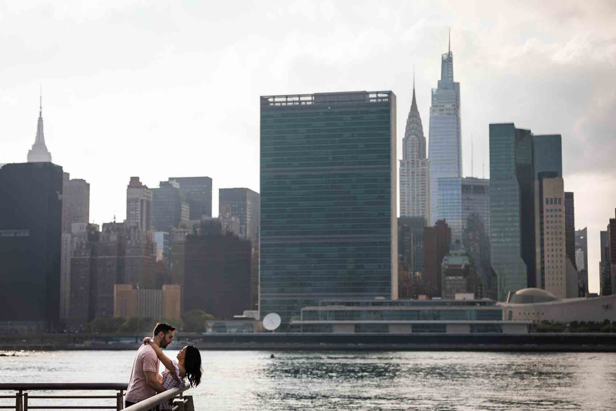 Couple leaning on railing in front of NYC waterfront during a Gantry Plaza State Park engagement photo shoot