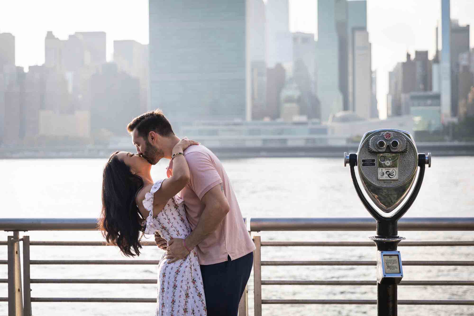 Couple kissing beside viewfinder during a Gantry Plaza State Park engagement photo shoot