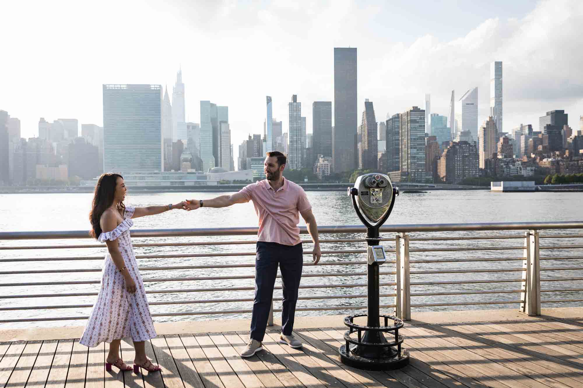 Couple dancing on boardwalk beside viewfinder during a Gantry Plaza State Park engagement photo shoot