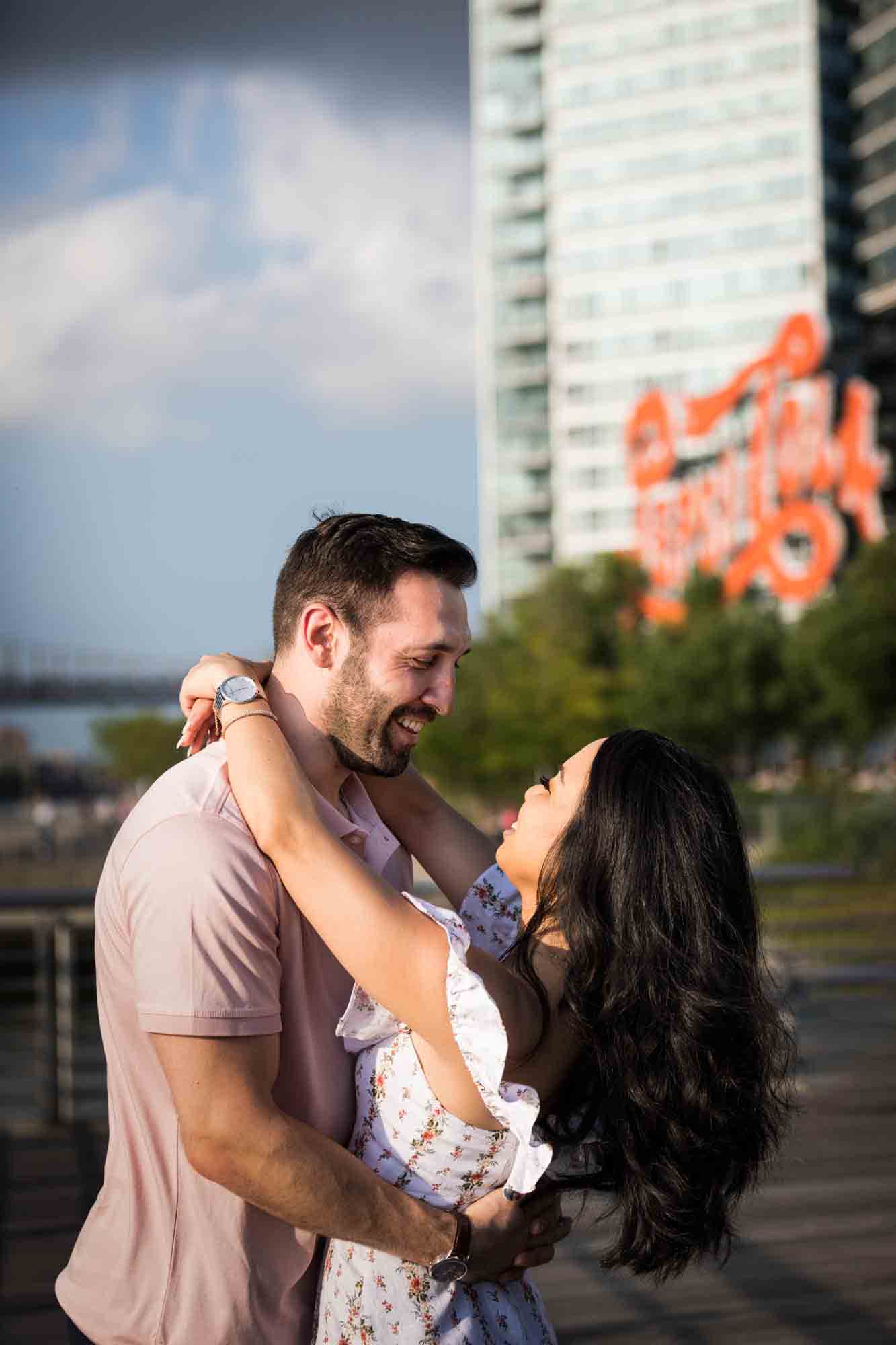 Couple hugging with Pepsi Cola sign in background during a Gantry Plaza State Park engagement photo shoot
