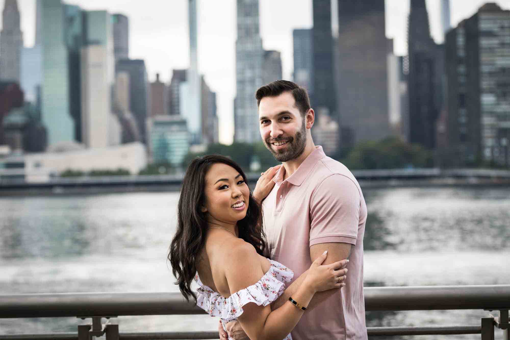 Couple hugging in front of NYC waterfront during a Gantry Plaza State Park engagement photo shoot