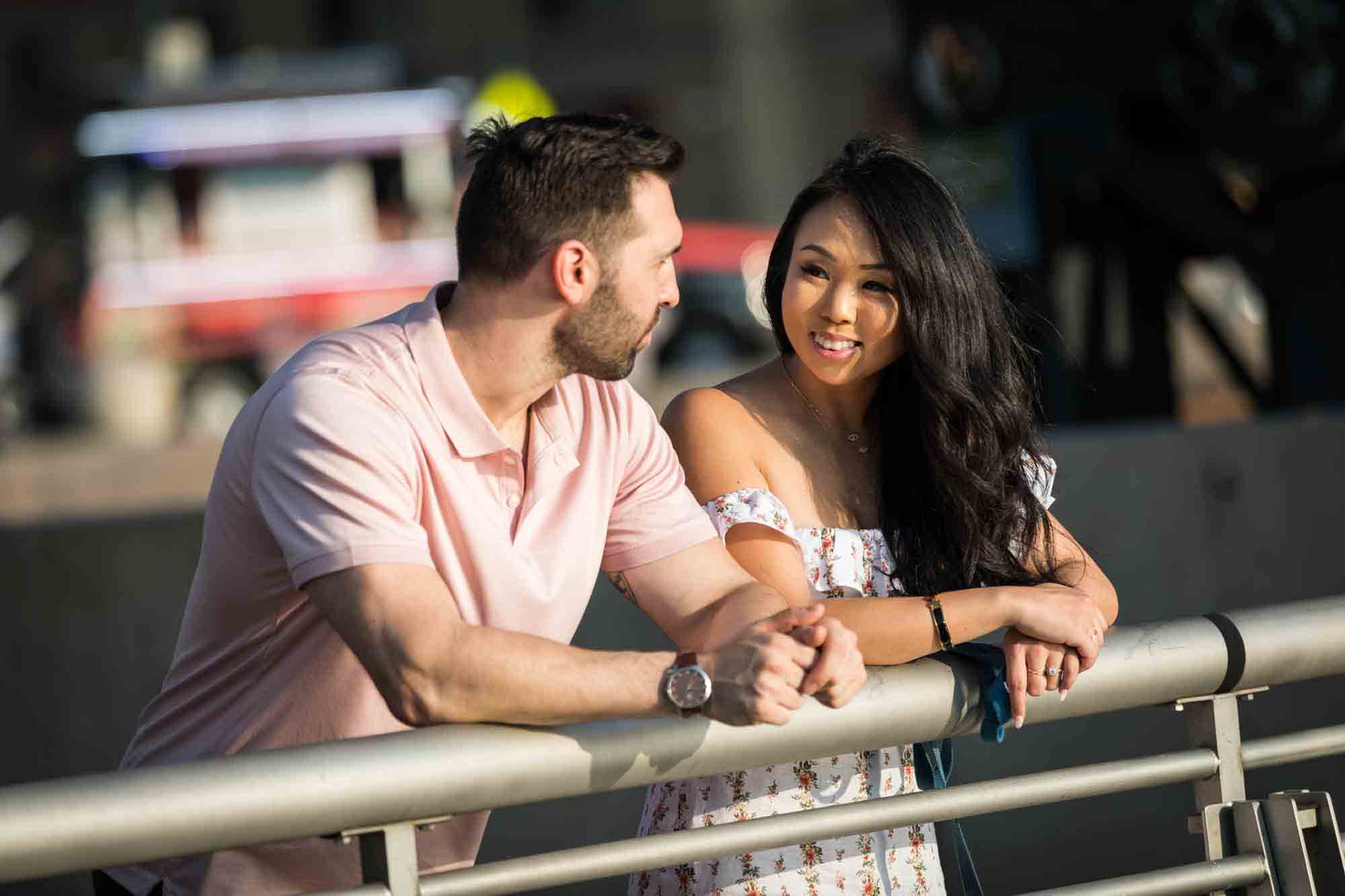 Couple leaning against railing and chatting during a Gantry Plaza State Park engagement photo shoot