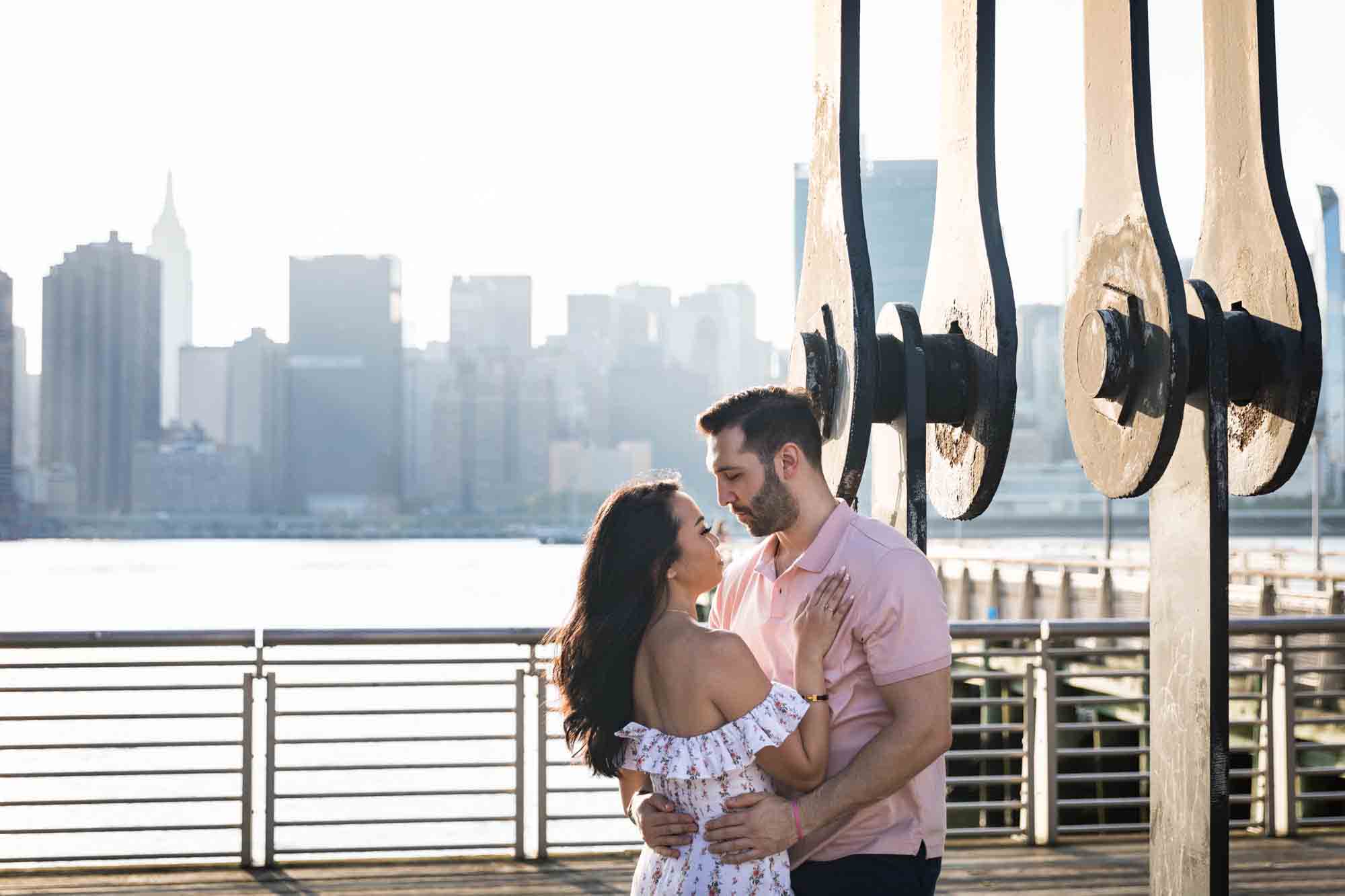 Couple hugging against gantry at sunset during a Gantry Plaza State Park engagement photo shoot