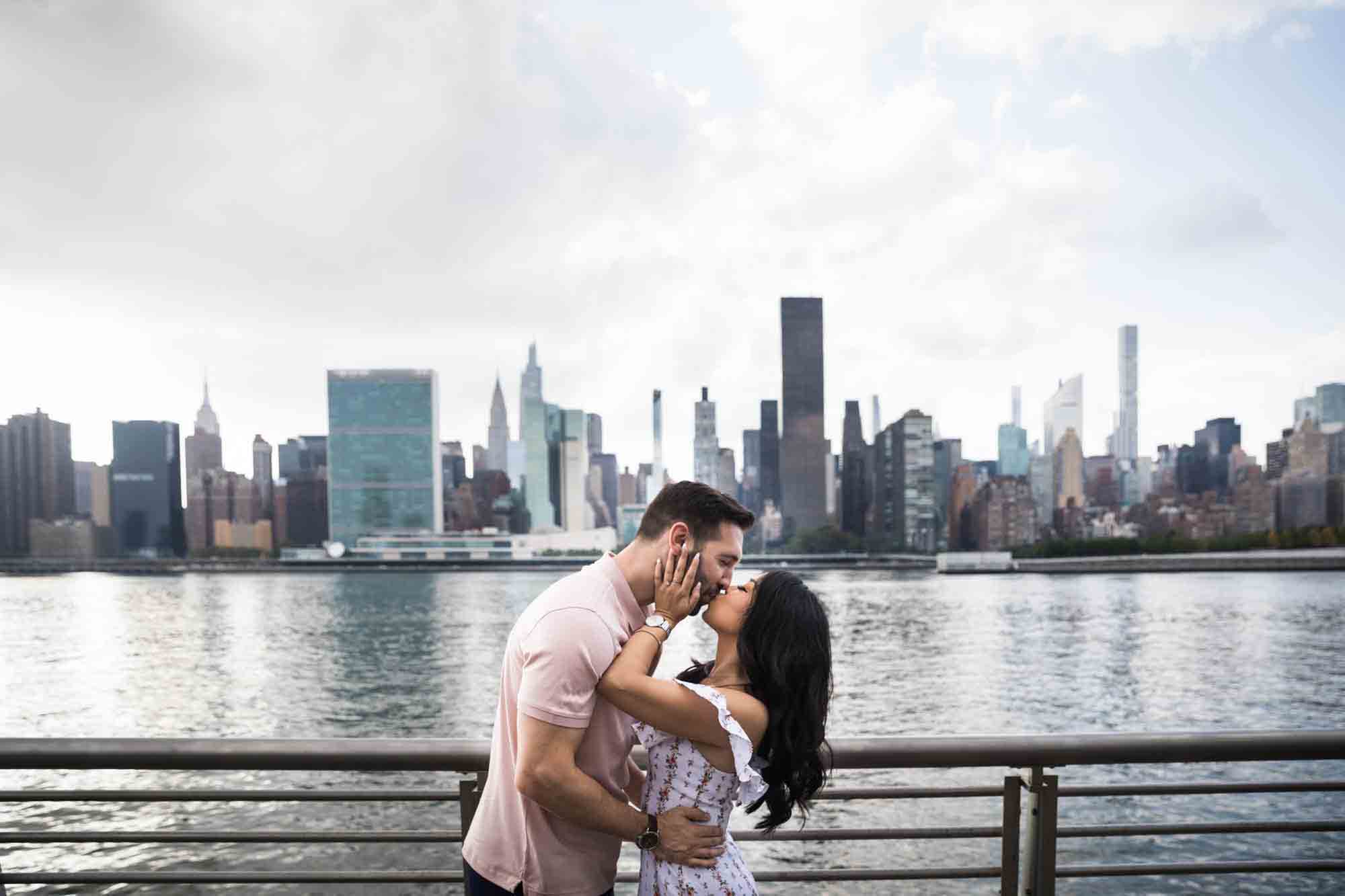Couple kissing in front of NYC waterfront during a Gantry Plaza State Park engagement photo shoot