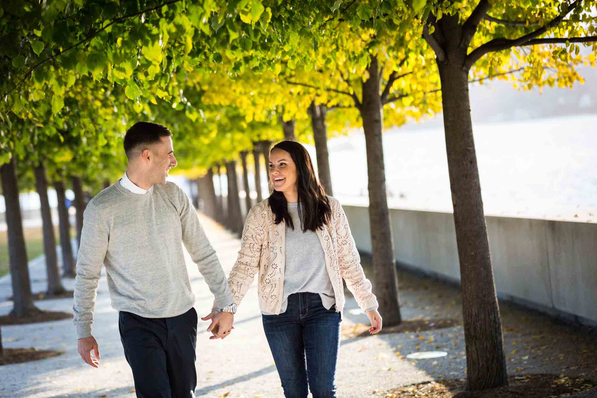 Couple holding hands and walking under trees during a Four Freedoms Park engagement photo shoot