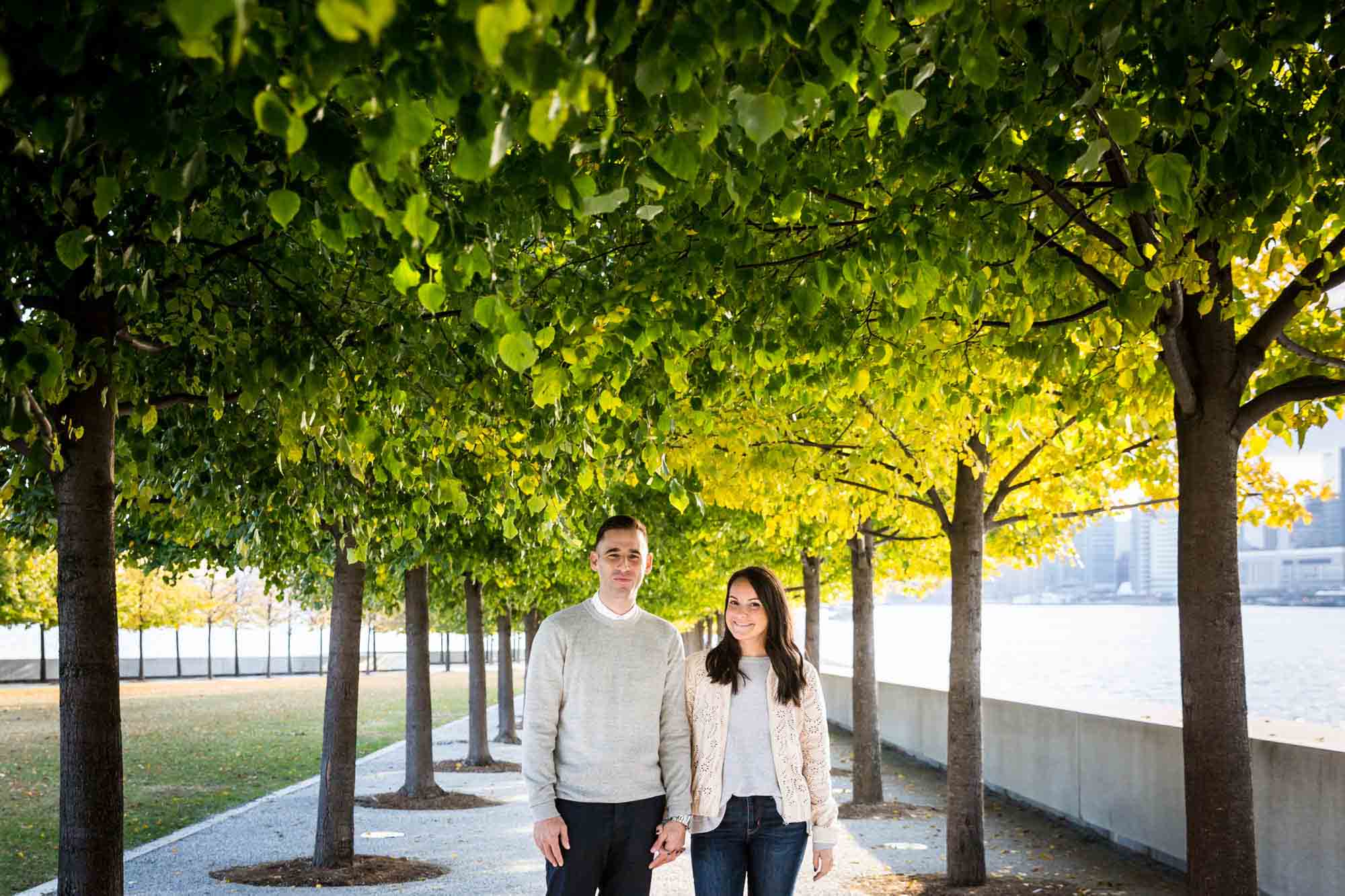 Couple holding hands standing under trees during a Four Freedoms Park engagement photo shoot