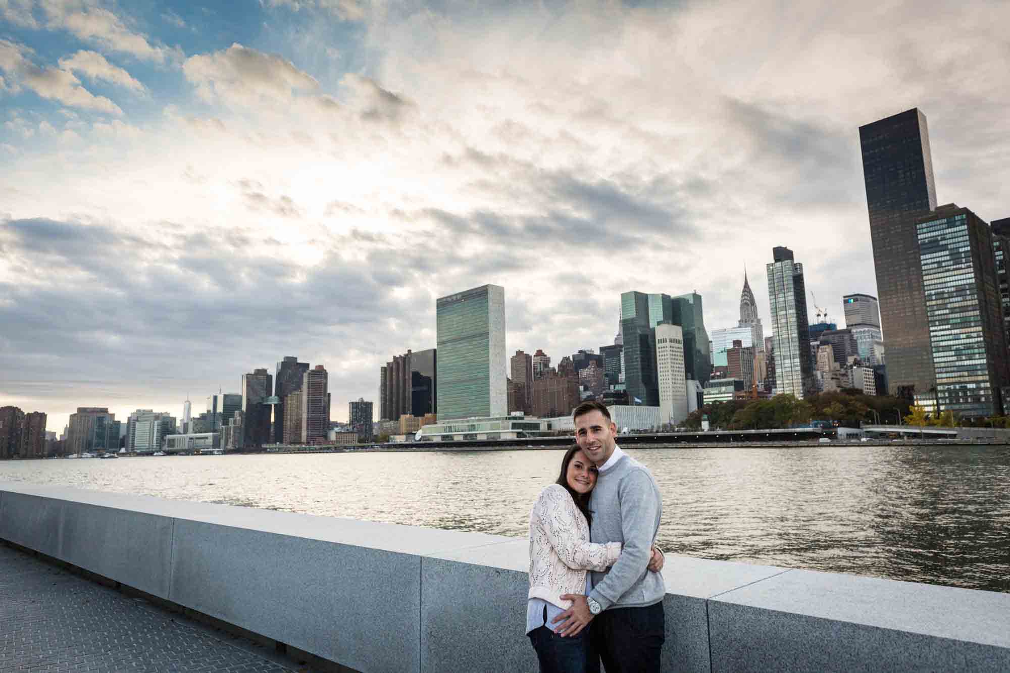 Couple hugging in front of NYC skyline during a Roosevelt Island engagement photo shoot