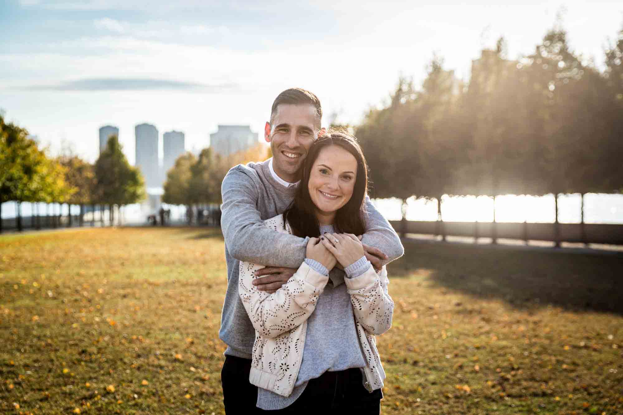 Couple hugging in front of grass during a Roosevelt Island engagement photo shoot