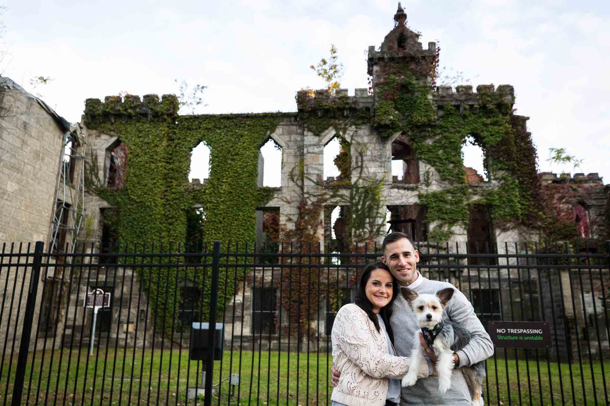 Couple holding dog in front of hospital ruins during a Roosevelt Island engagement photo shoot