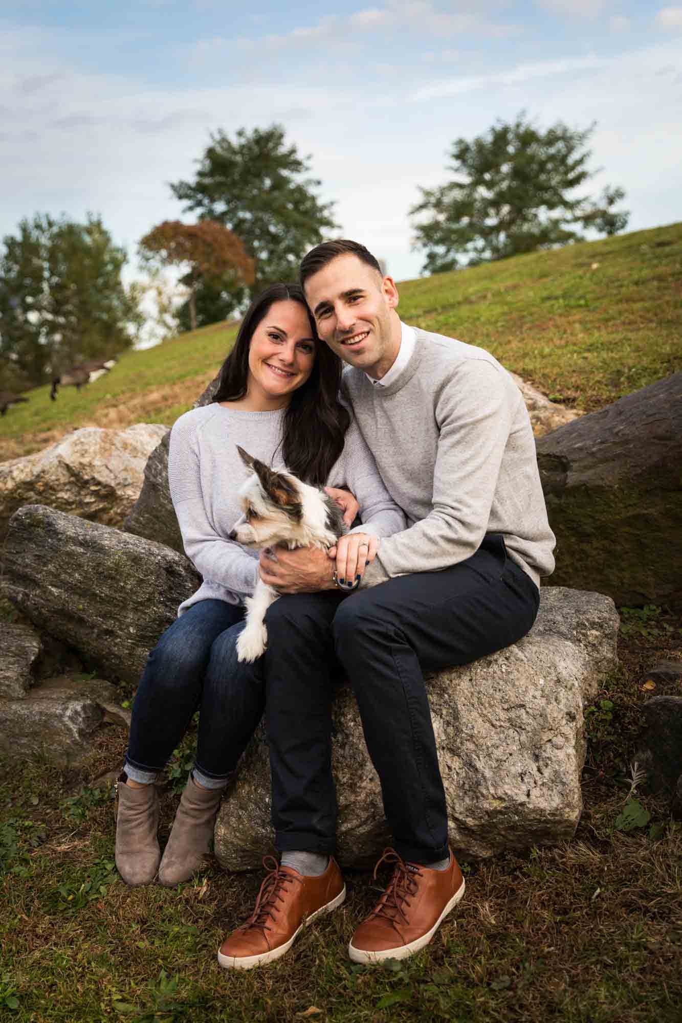 Couple sitting on rock holding dog for an article on pet engagement photo tips