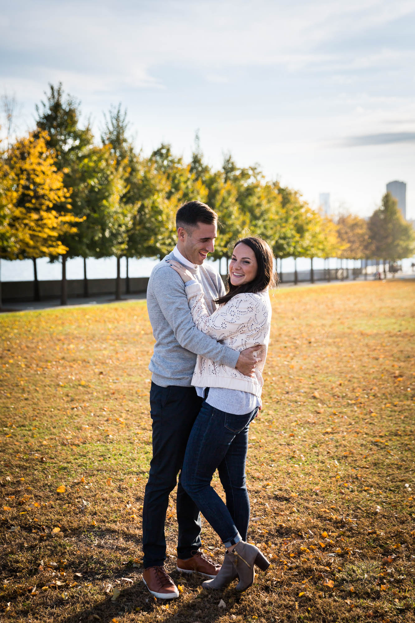 Couple hugging in front of grass and trees during a Roosevelt Island engagement photo shoot