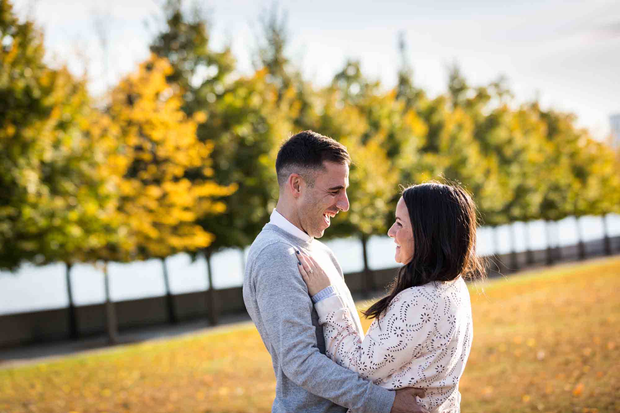 Woman with hands on man's chest in front of trees during a Roosevelt Island engagement photo shoot