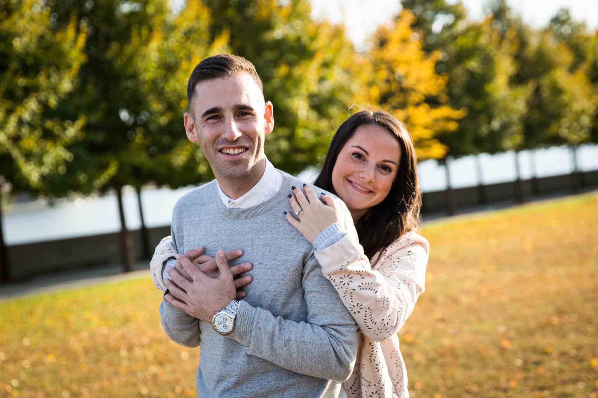 Couple hugging in front of trees during Roosevelt Island engagement shoot for an article on pet engagement photo tips