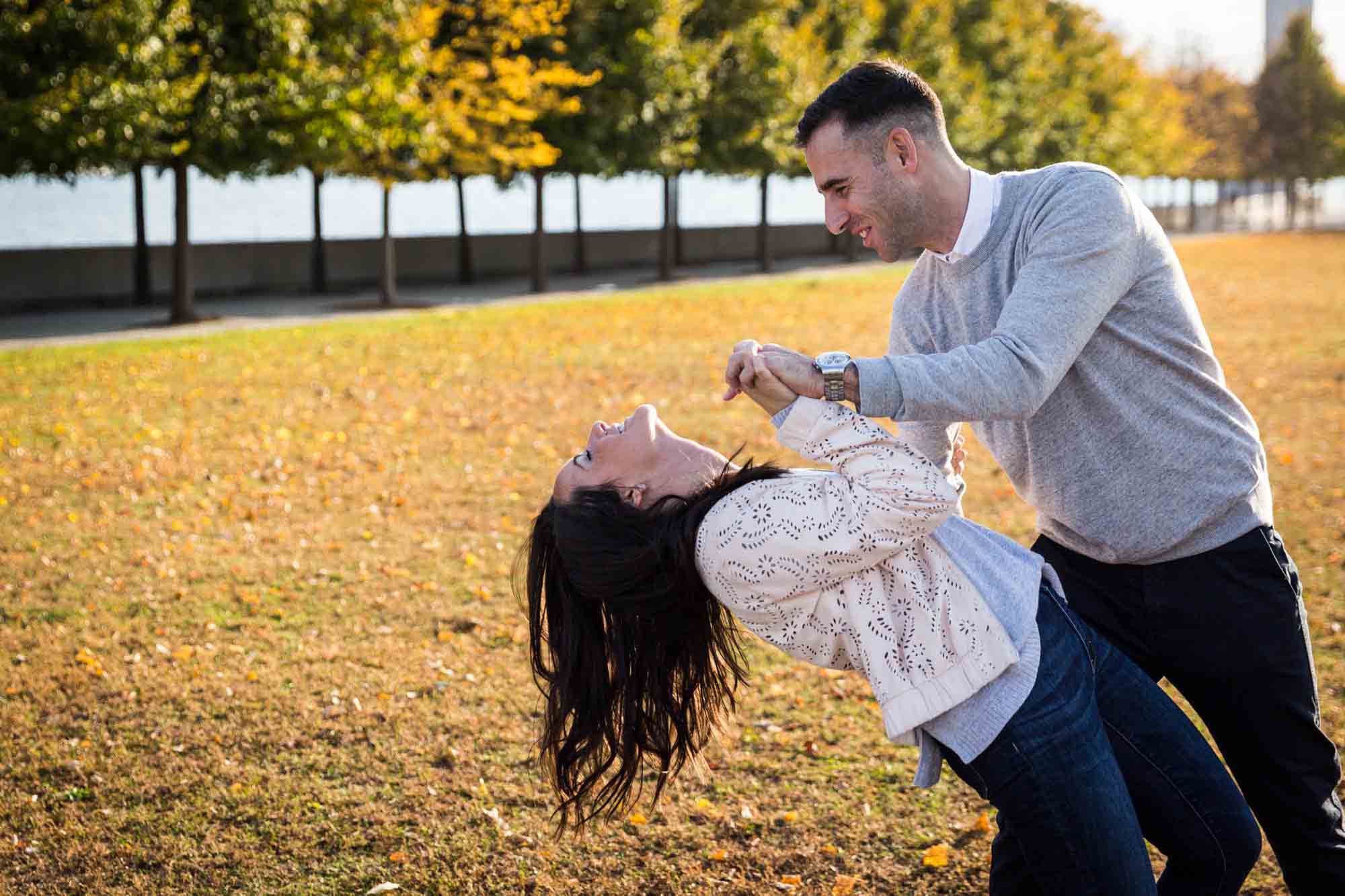 Man dipping woman while dancing in front of grass during a Roosevelt Island engagement photo shoot