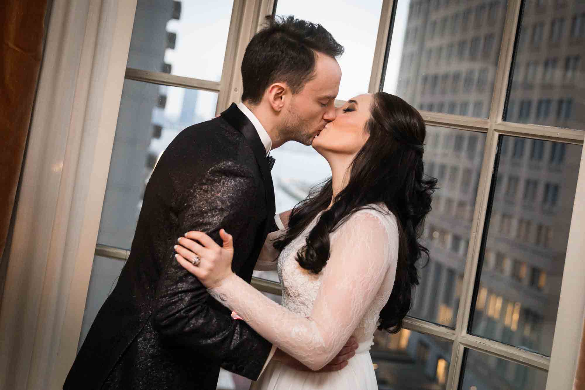 Bride and groom kissing in front of window