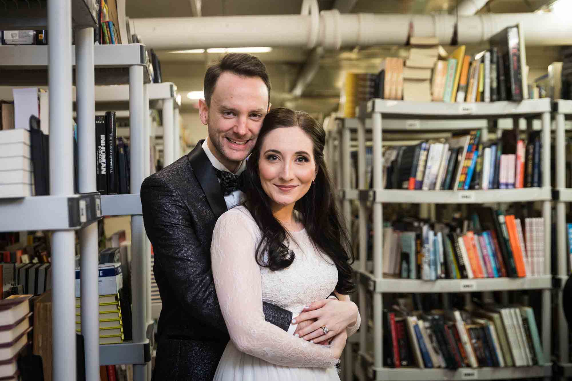 Bride and groom hugging in front of bookcases at a Housing Works Bookstore wedding