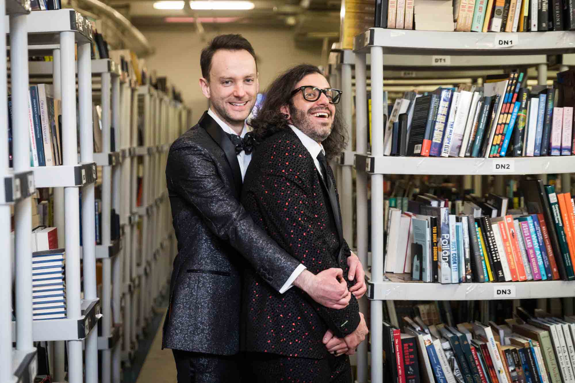 Groom and best man hugging in front of bookcases at a Housing Works Bookstore wedding