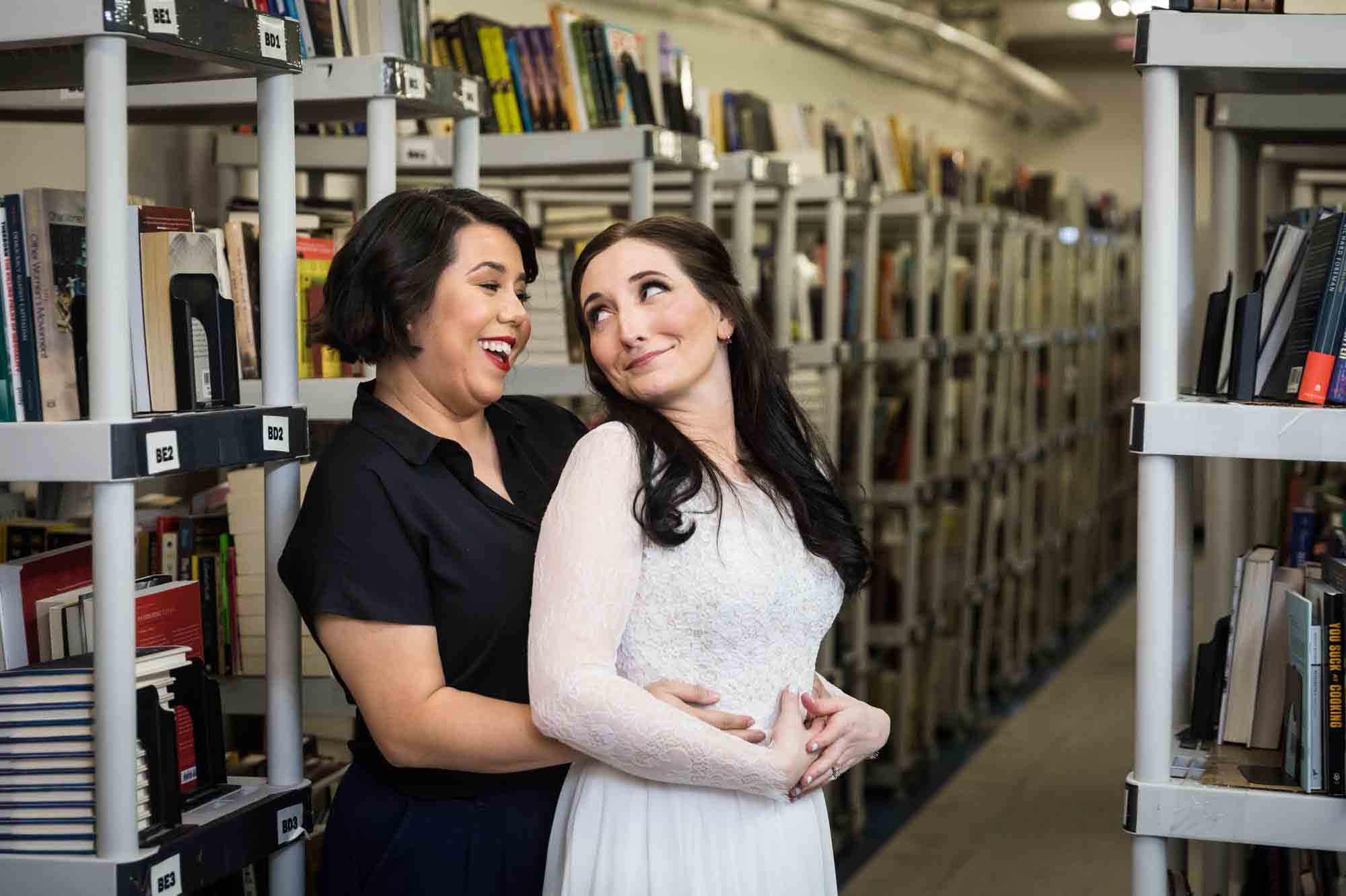 Bride and maid of honor hugging in front of bookcases at a Housing Works Bookstore wedding
