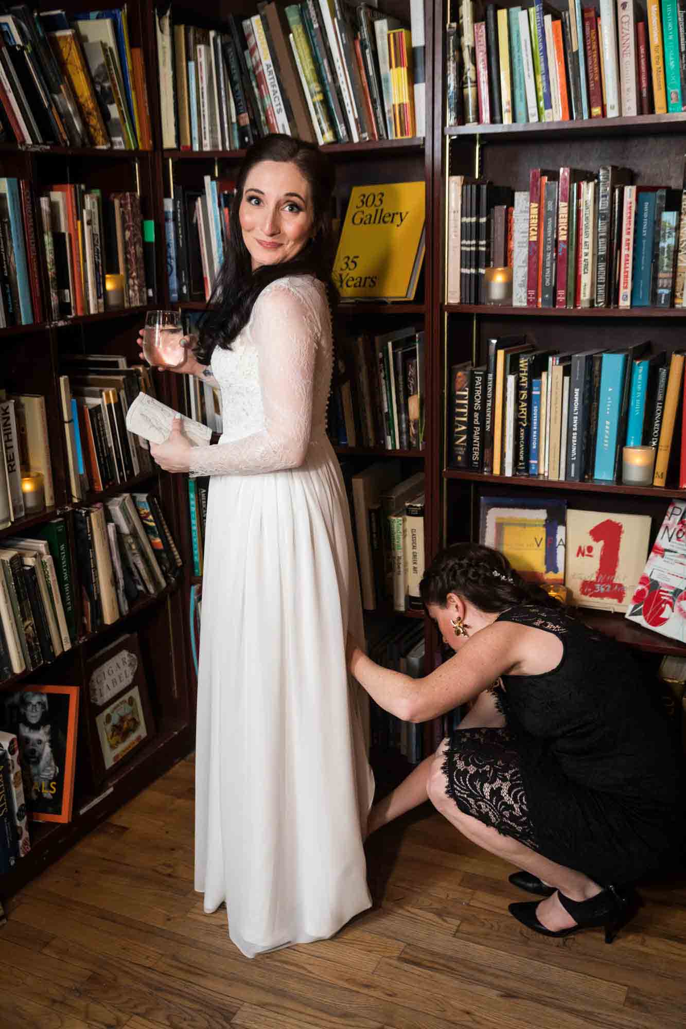 Bride in front of bookcase having her dress bustled for an article on wedding ceremony photo tips
