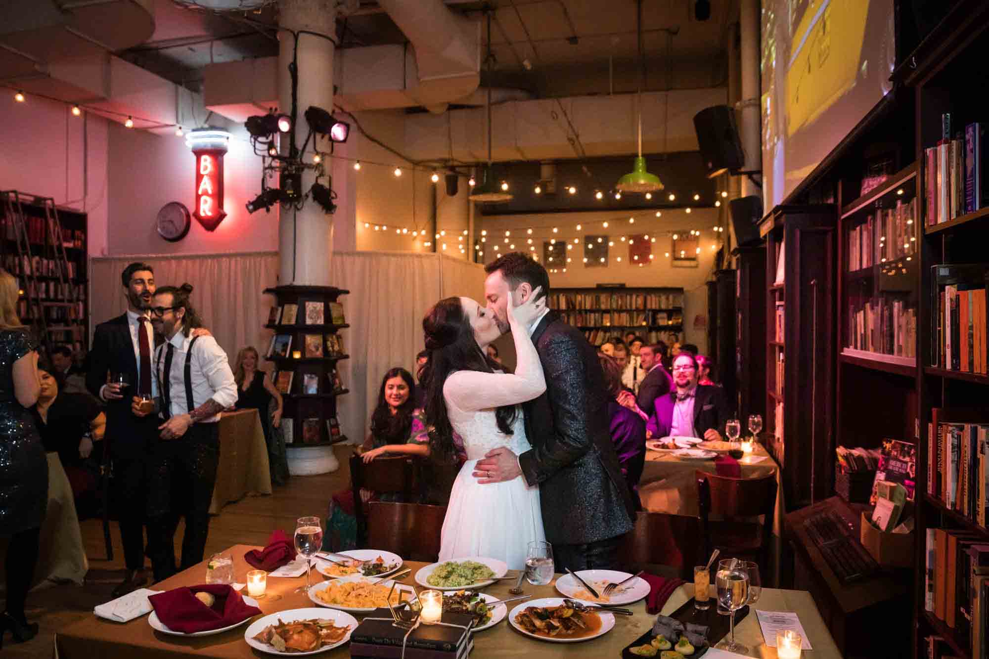 Bride and groom kissing behind table at a Housing Works Bookstore wedding